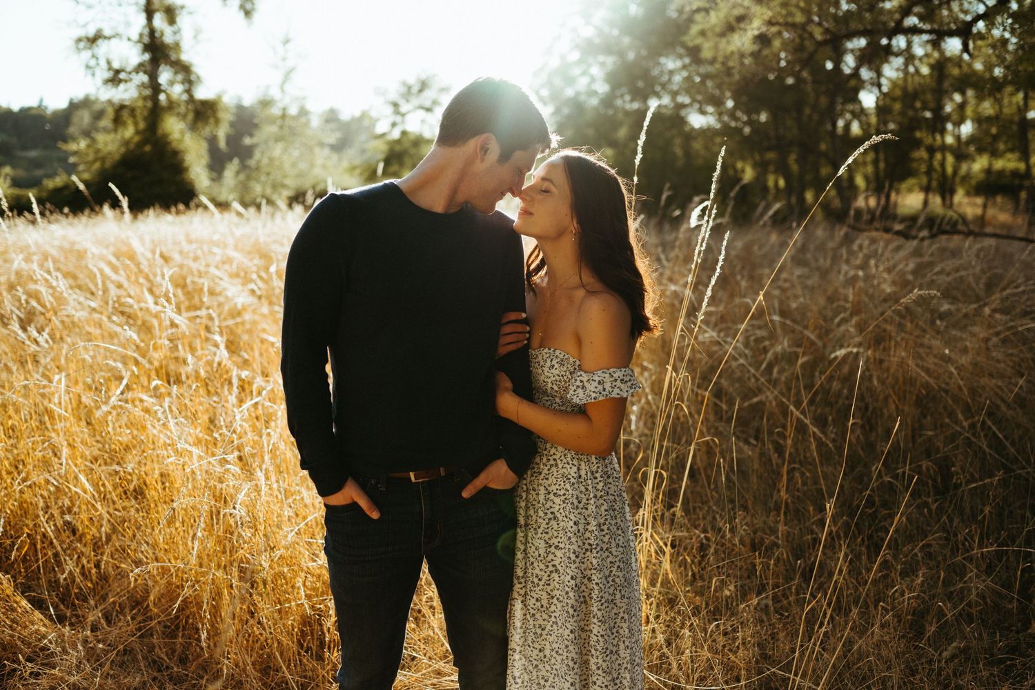 Couple embracing in golden field during sunset with dramatic lighting.