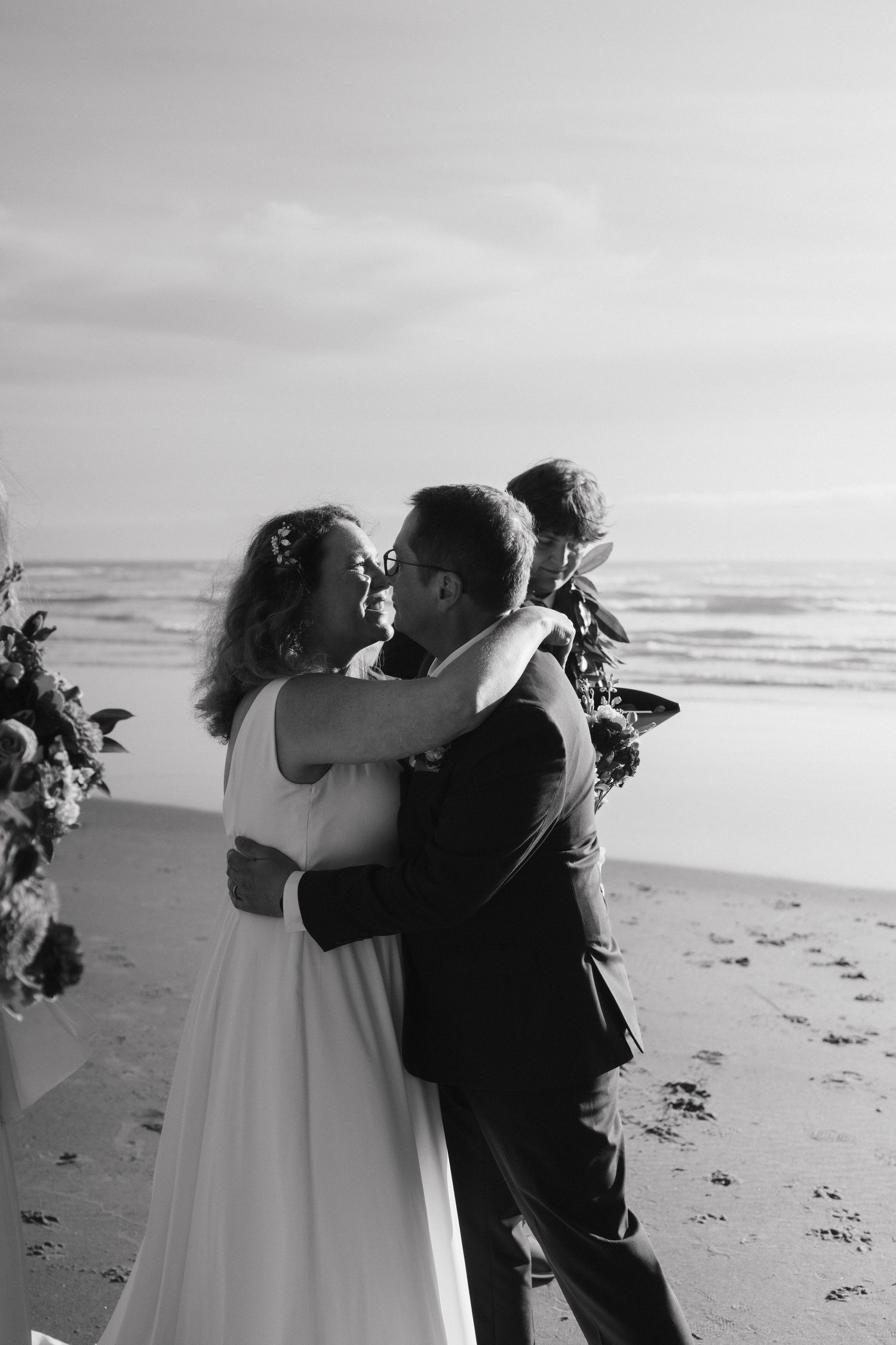 A romantic black and white beach wedding photo of a couple embracing.