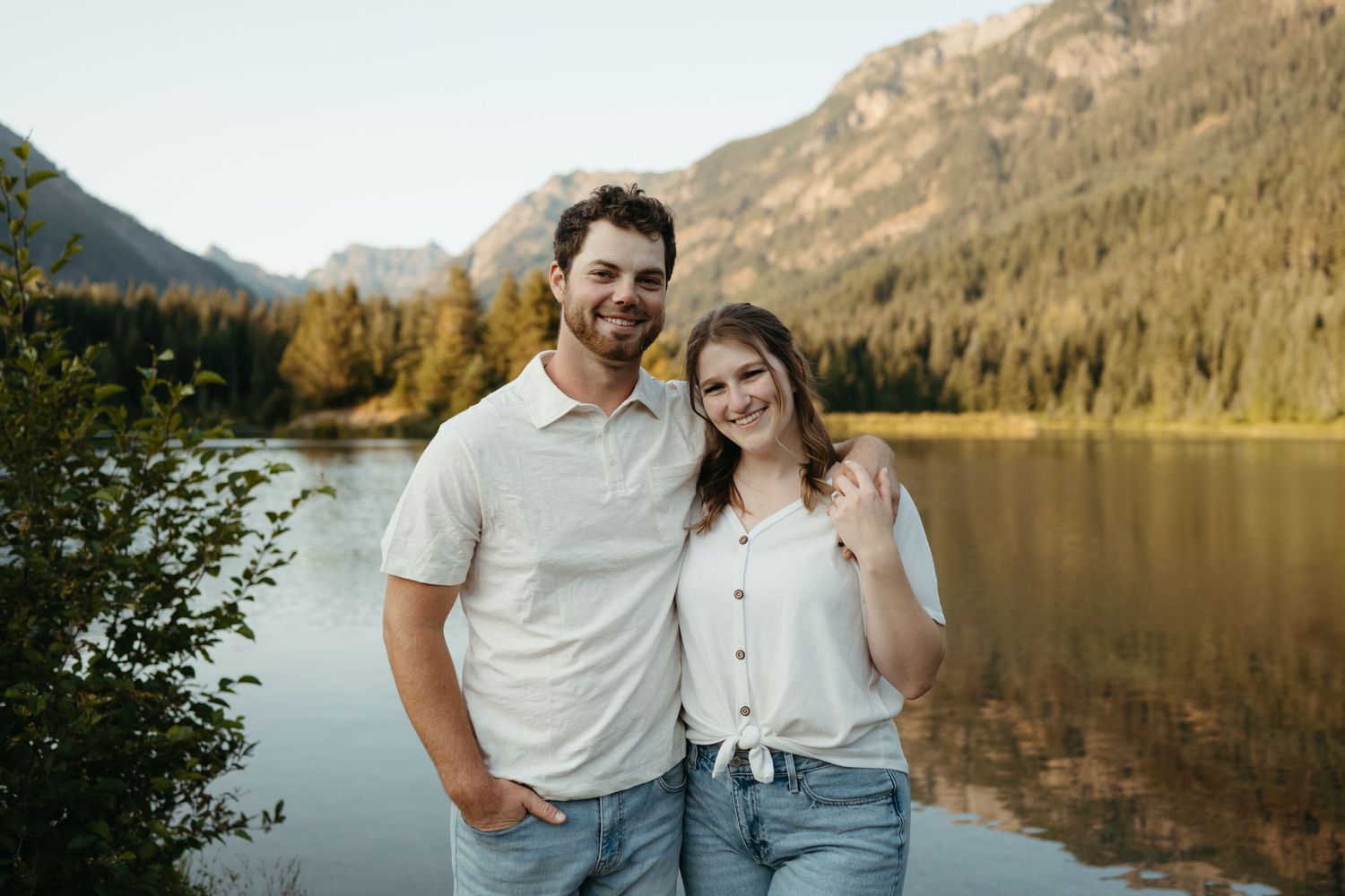 Happy couple posing together by scenic mountain lake during golden hour.