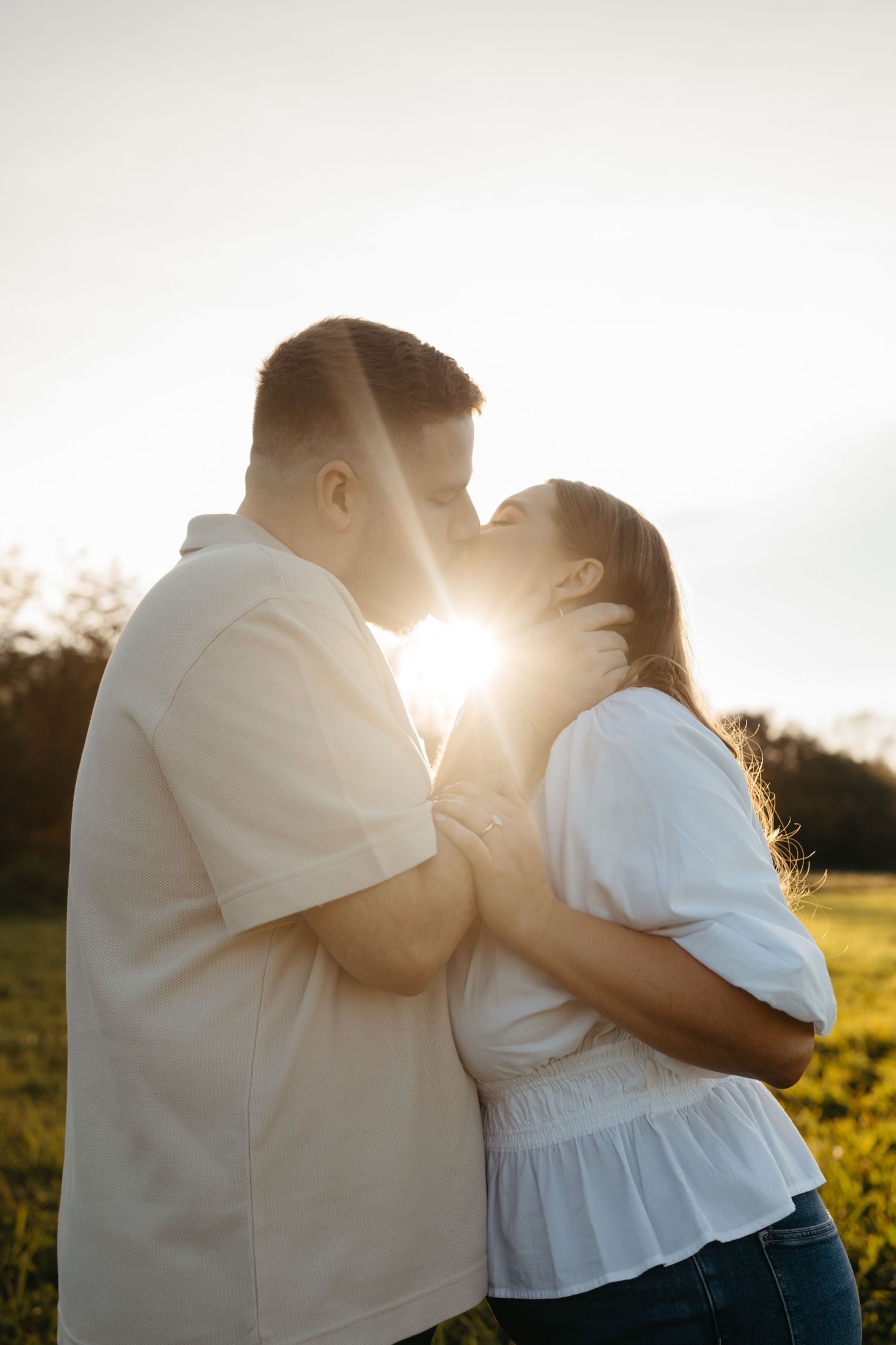 Backlit couple sharing intimate moment with sun flare during golden hour portrait session.