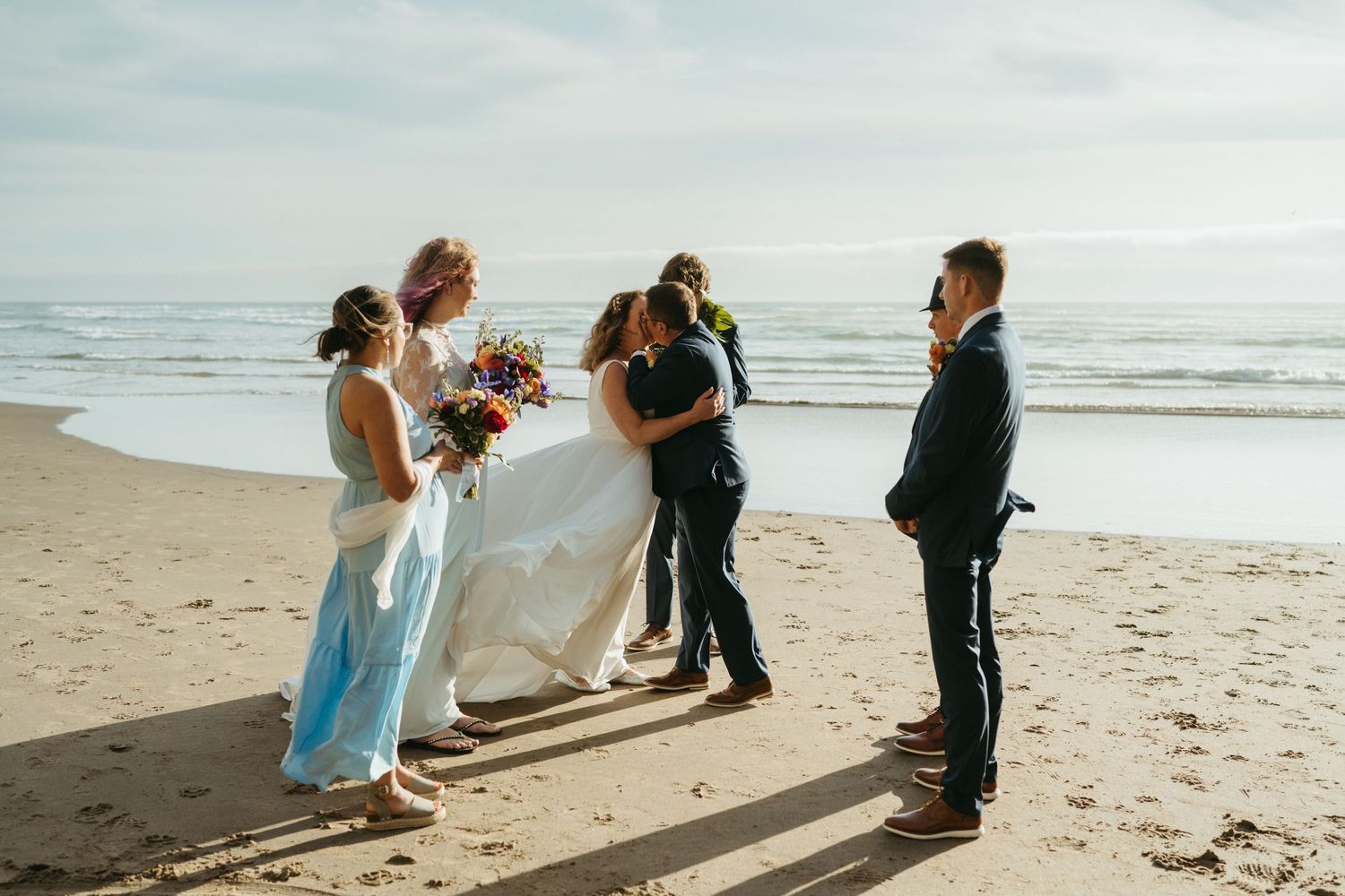 A wedding ceremony taking place on a sunny beach with attendants gathered around the couple.