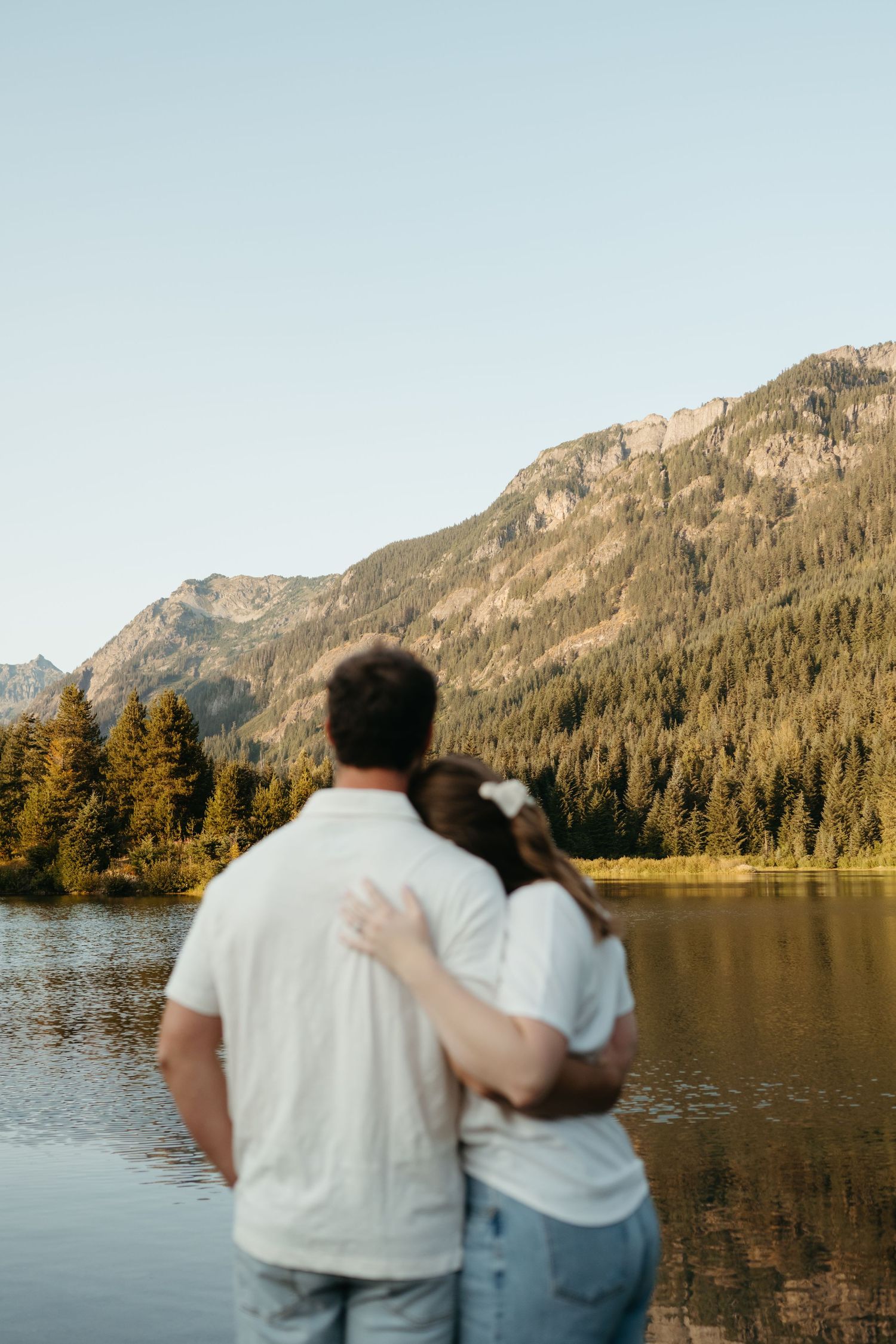Couple embracing while overlooking peaceful mountain lake at sunset.