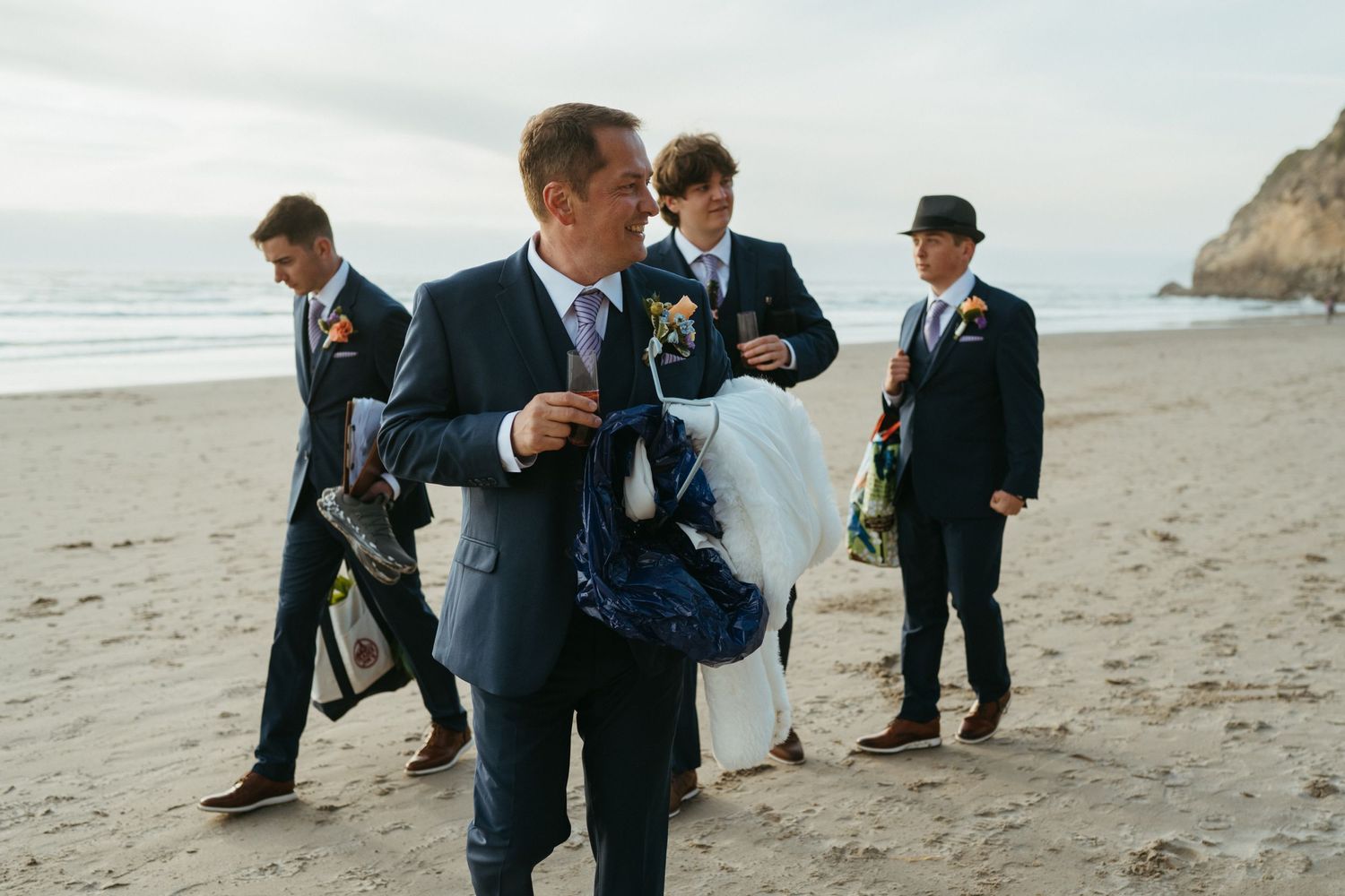 Wedding party members gathered on a beach with dramatic coastal cliffs in the background.
