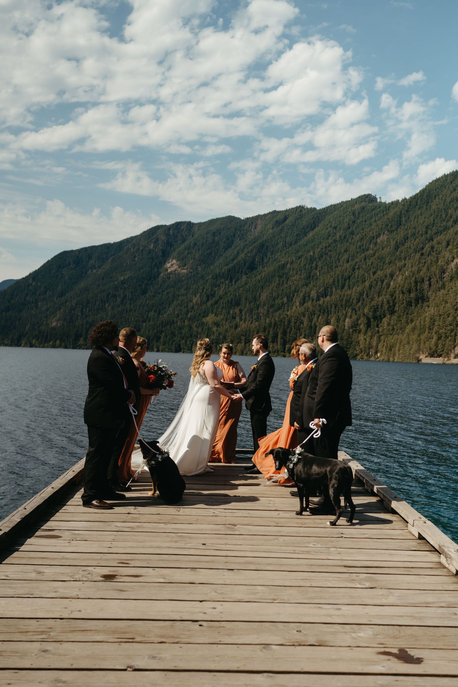 Wedding ceremony on wooden dock overlooking mountain lake with guests and blue skies.