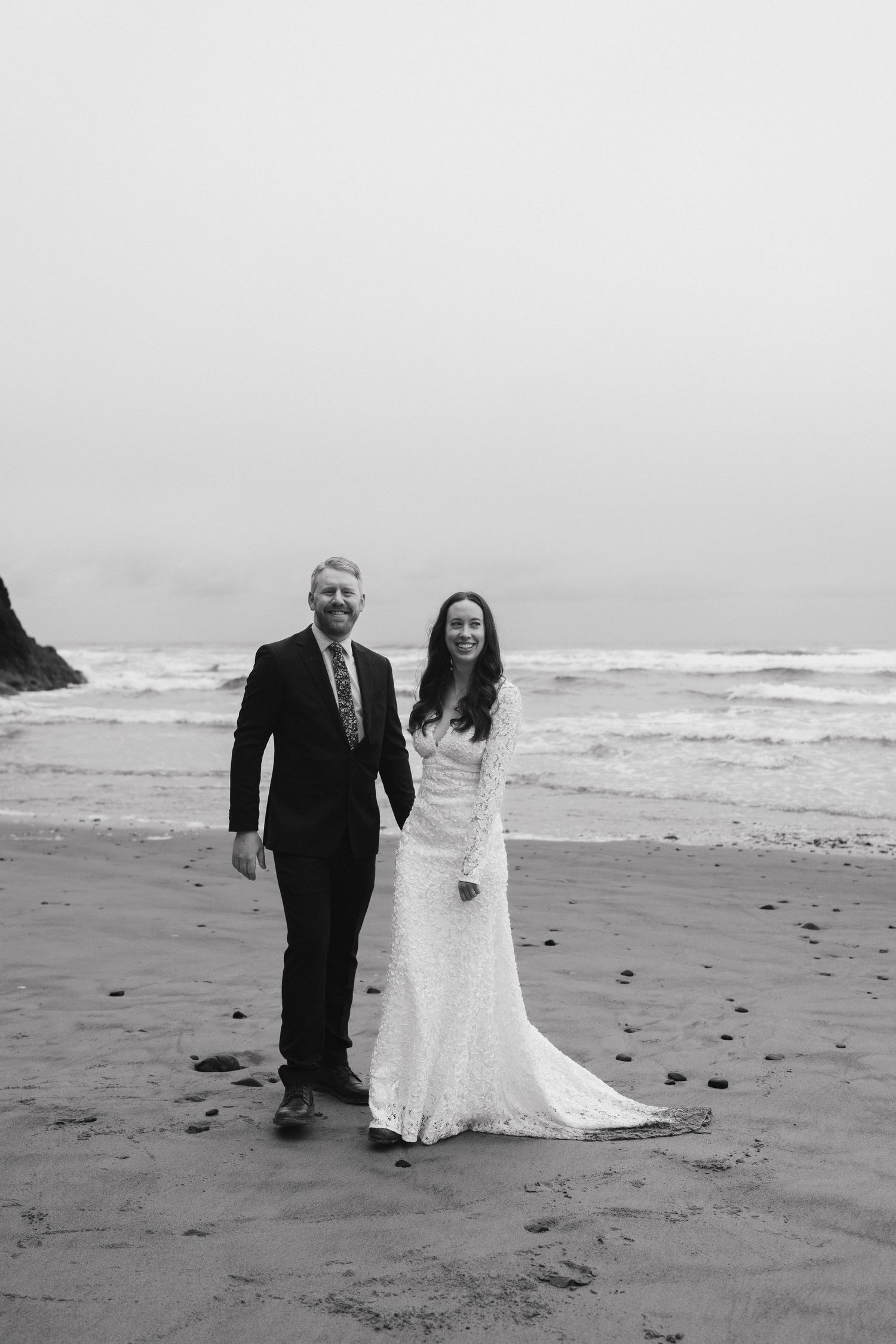 A black and white portrait of a couple walking on a misty beach after their wedding ceremony.