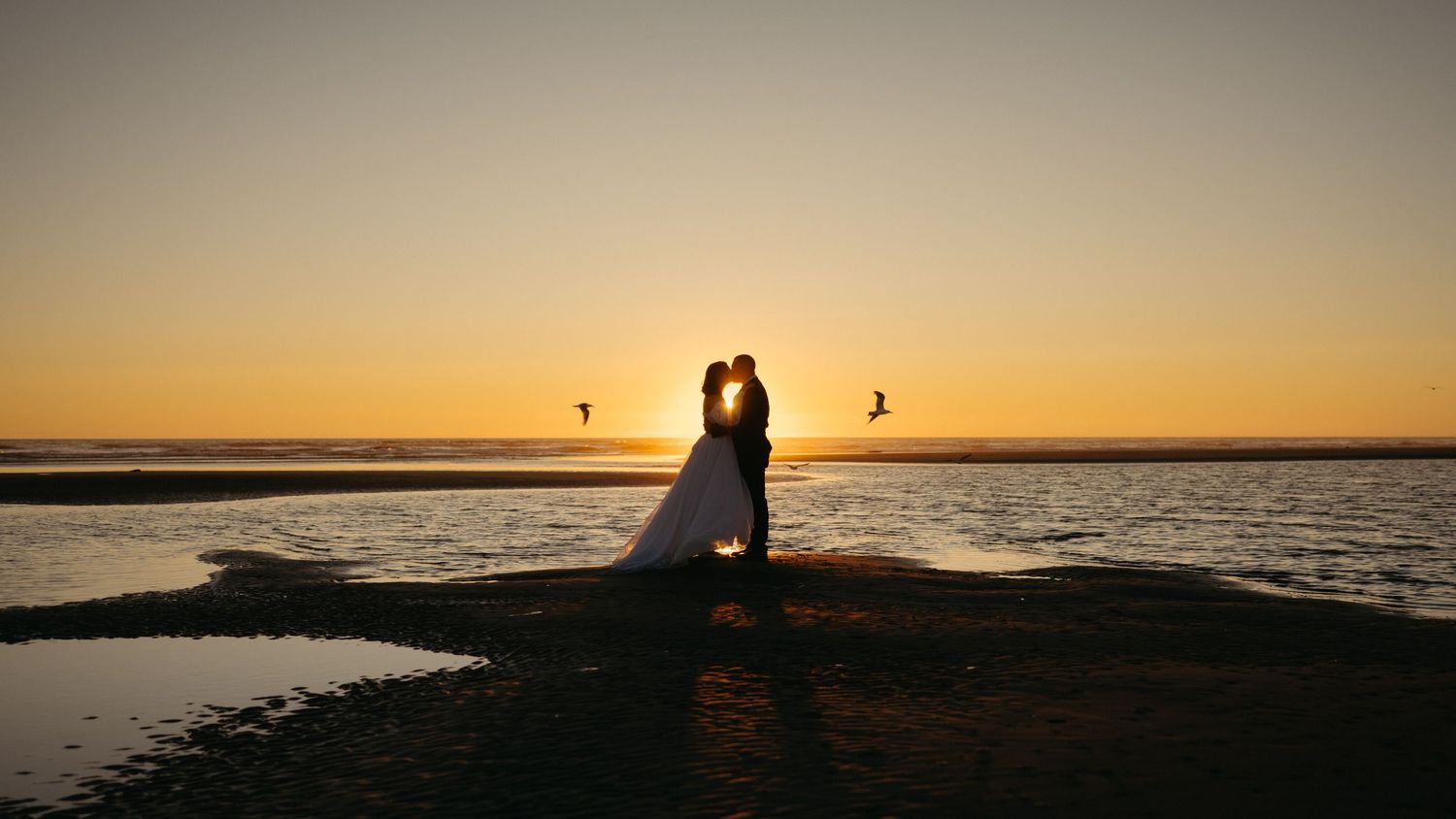 Silhouetted figures against a vibrant sunset sky over a peaceful beach.