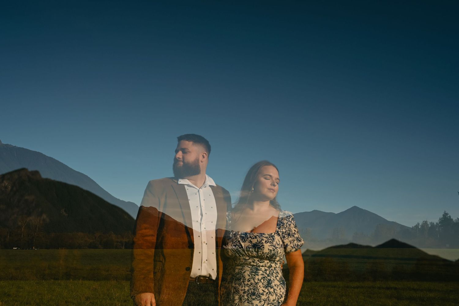 Couple poses together against mountain landscape during blue hour with artistic double exposure effect.