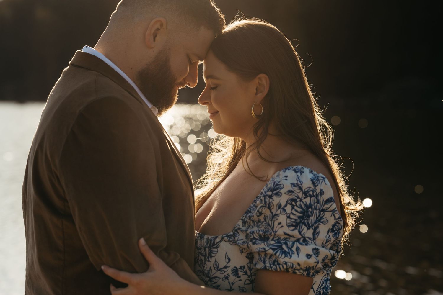 A romantic sunset portrait of a couple in close embrace by a lakeside.