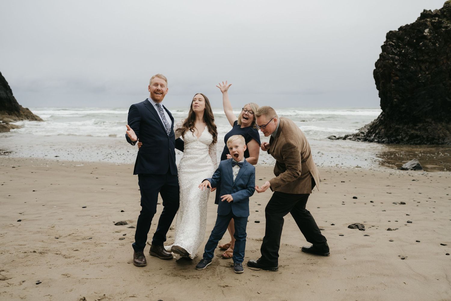A playful group photo of wedding attendees on a beach with dramatic coastal rocks.