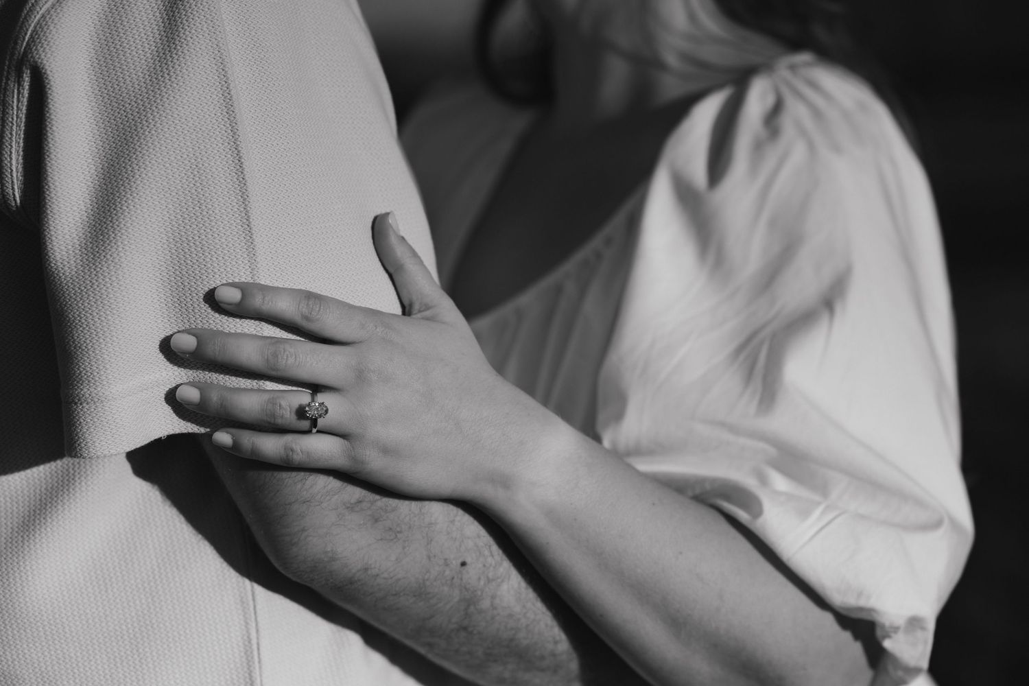 Close-up black and white shot of hands embracing with an engagement ring visible.