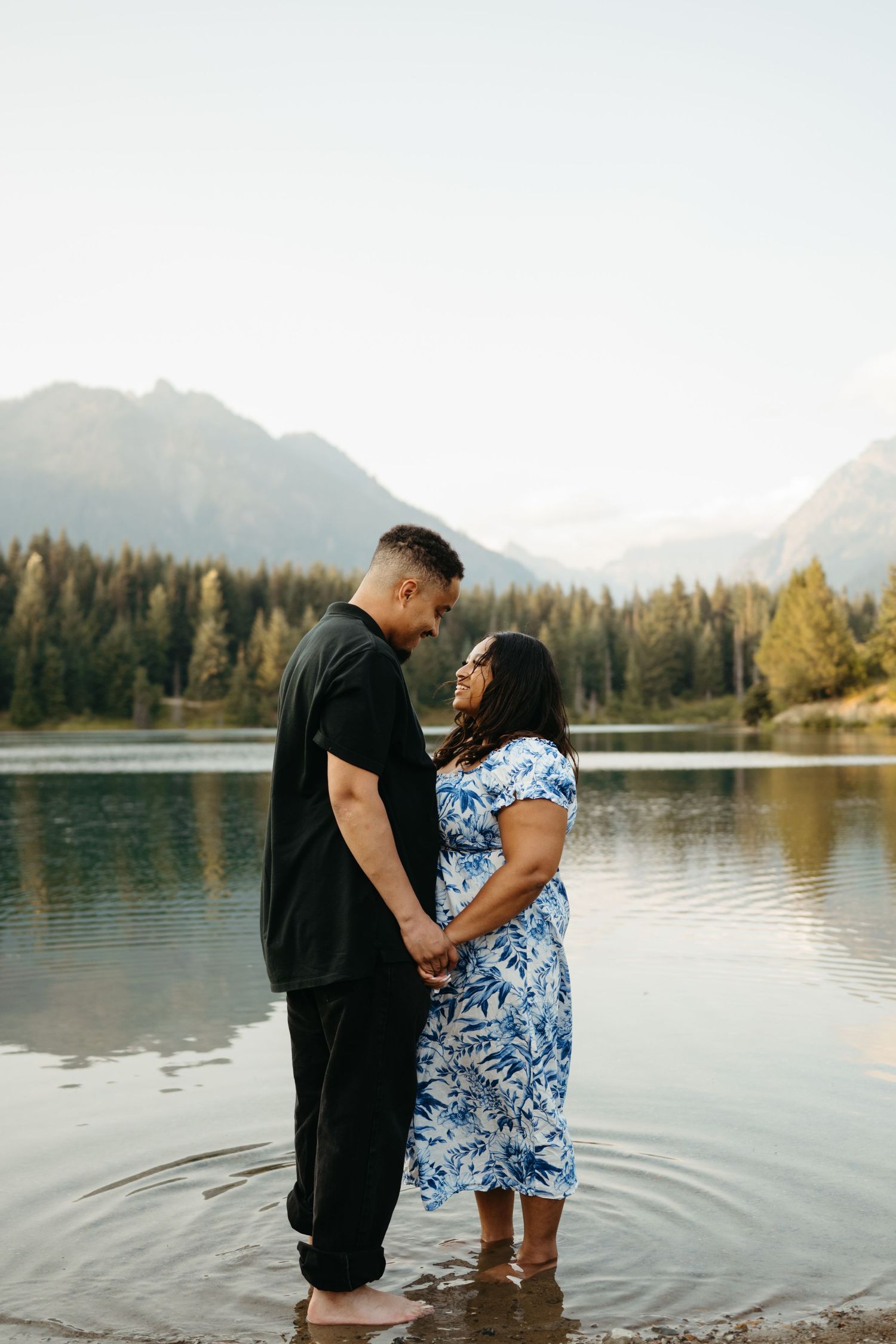A couple shares an intimate moment by a mountain lake during sunset.