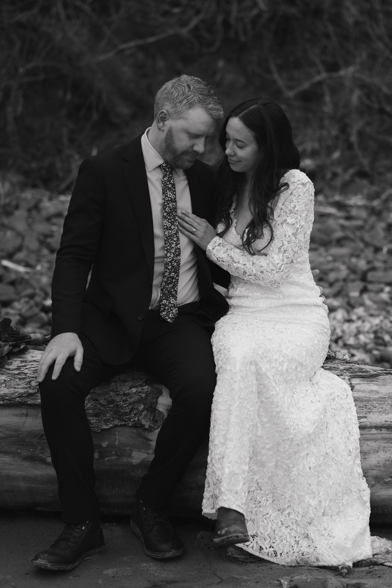 Intimate black and white portrait of a couple sitting on a log together.
