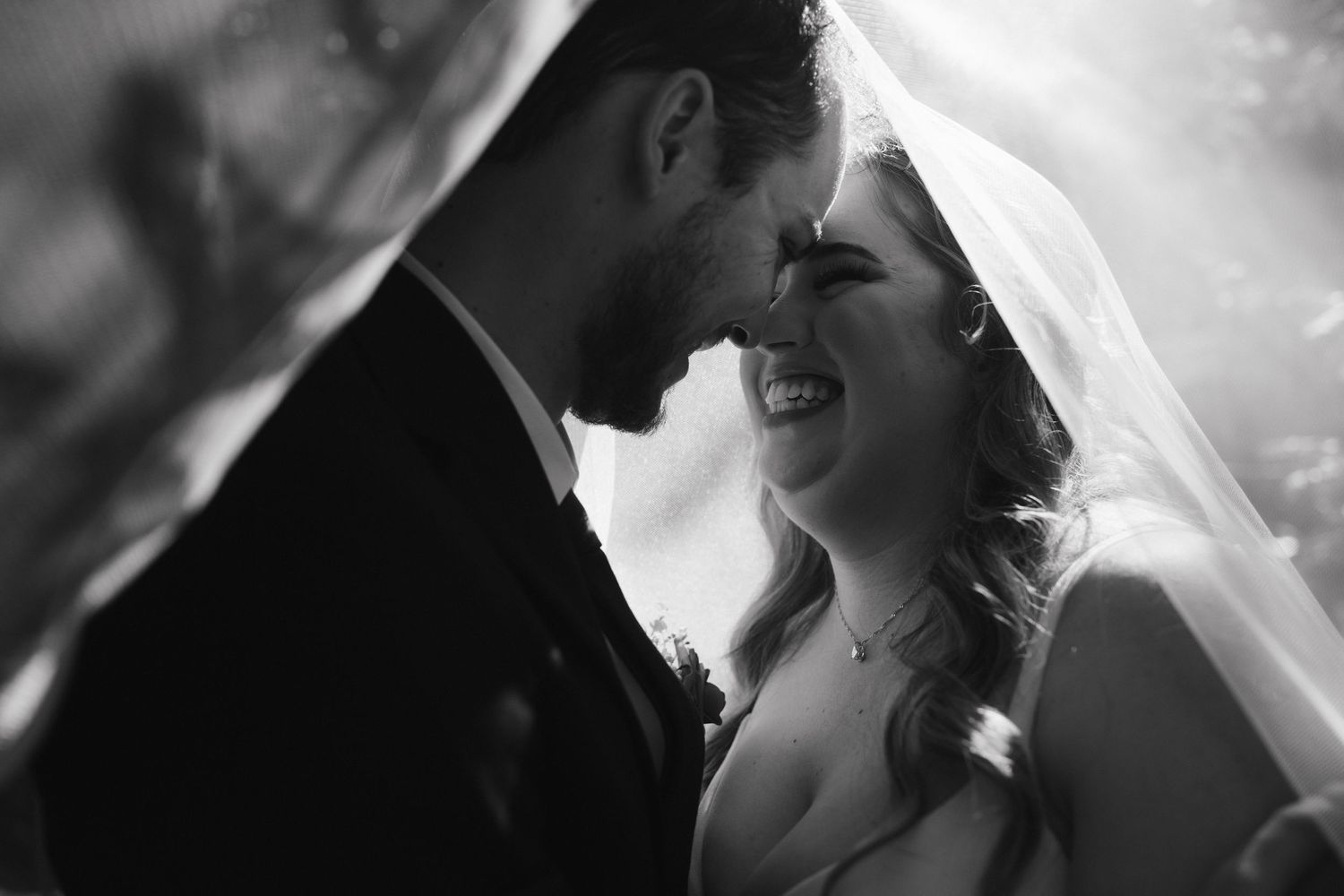 An intimate black and white portrait of a joyful wedding moment under a veil.