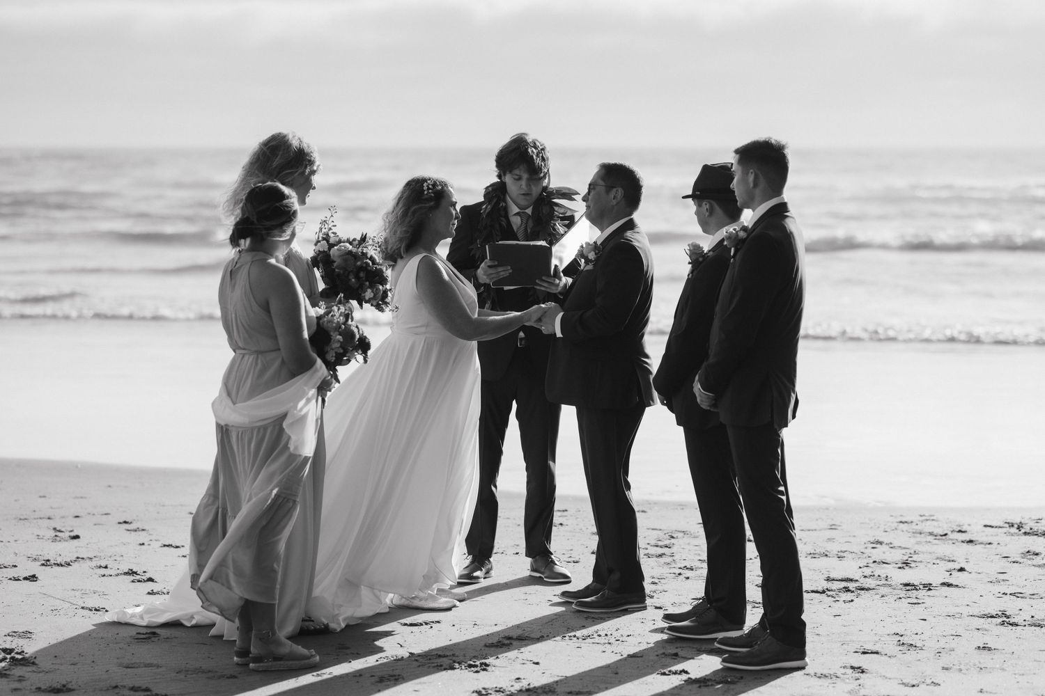 A black and white photo of a wedding ceremony taking place on a sunny beach.