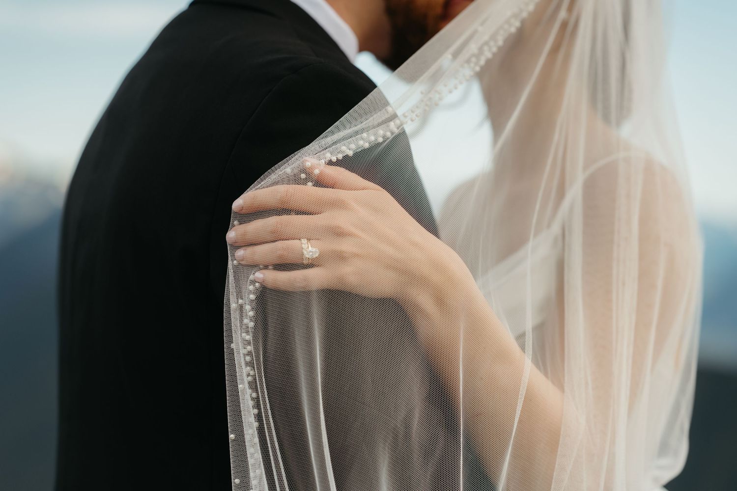 Close-up of bride's hand on groom's shoulder with delicate lace veil detail.