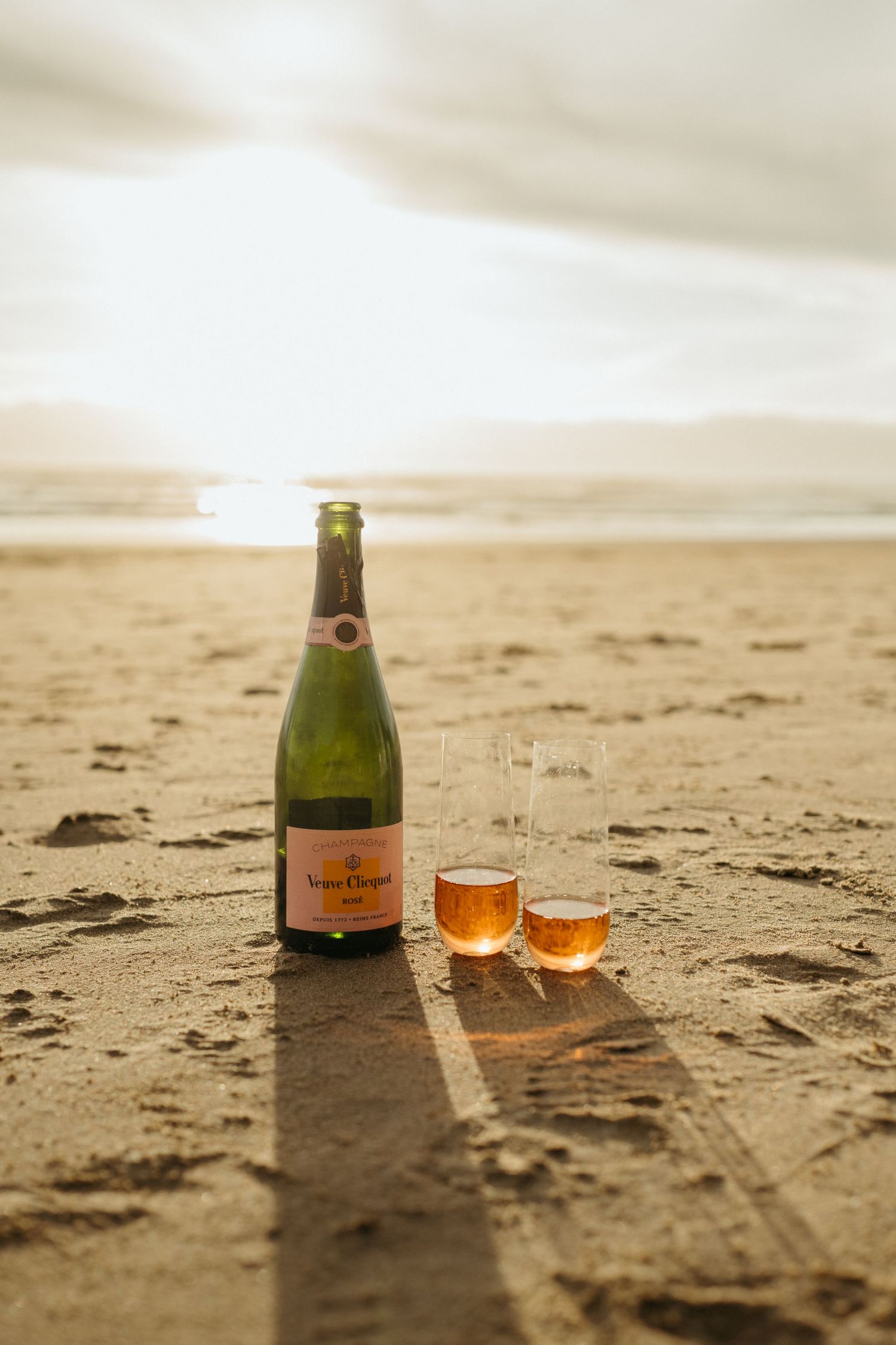 Champagne and glasses set up for a romantic beach celebration at sunset.