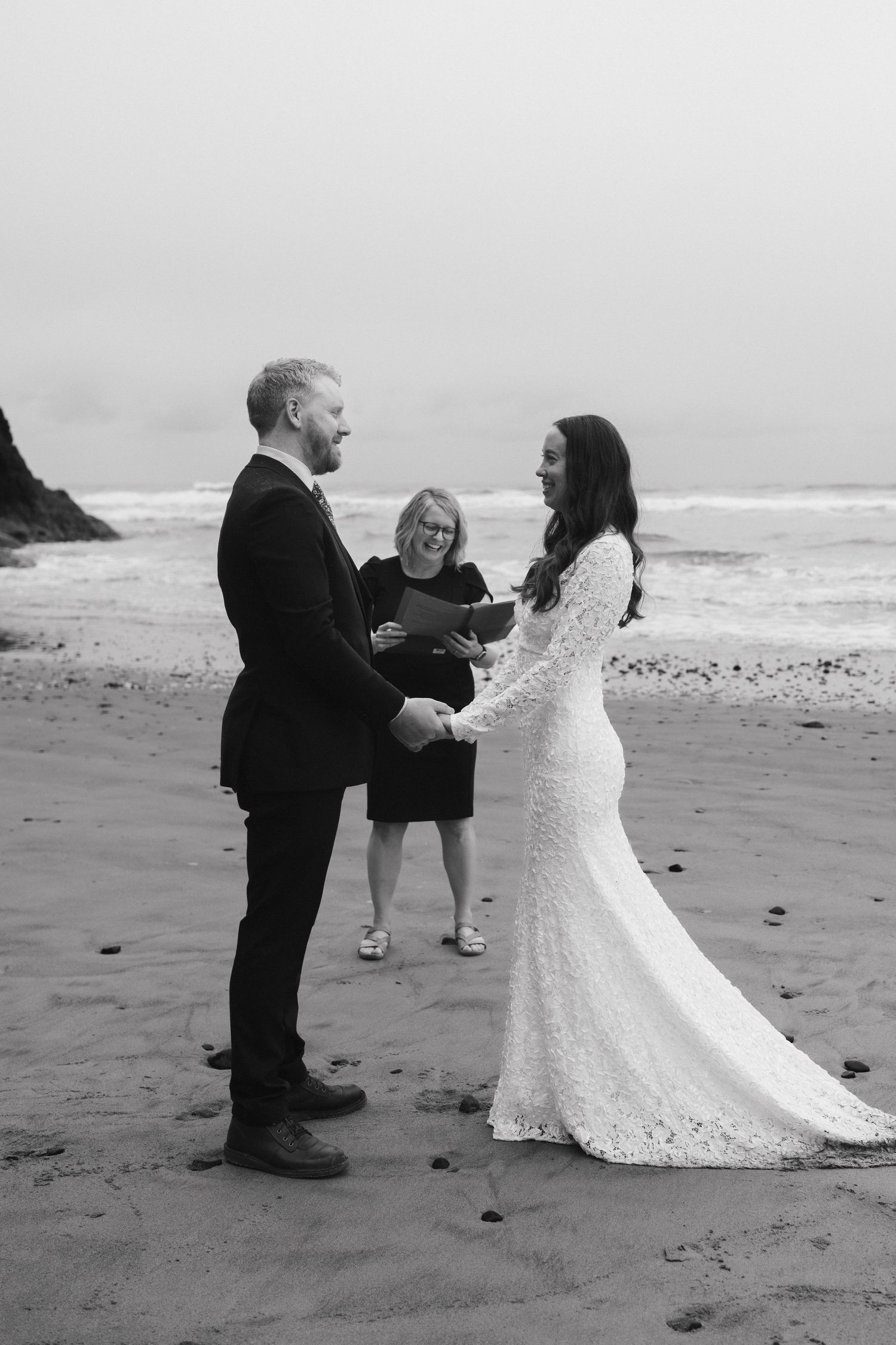 A black and white photo of a beach wedding ceremony with waves crashing in the background.