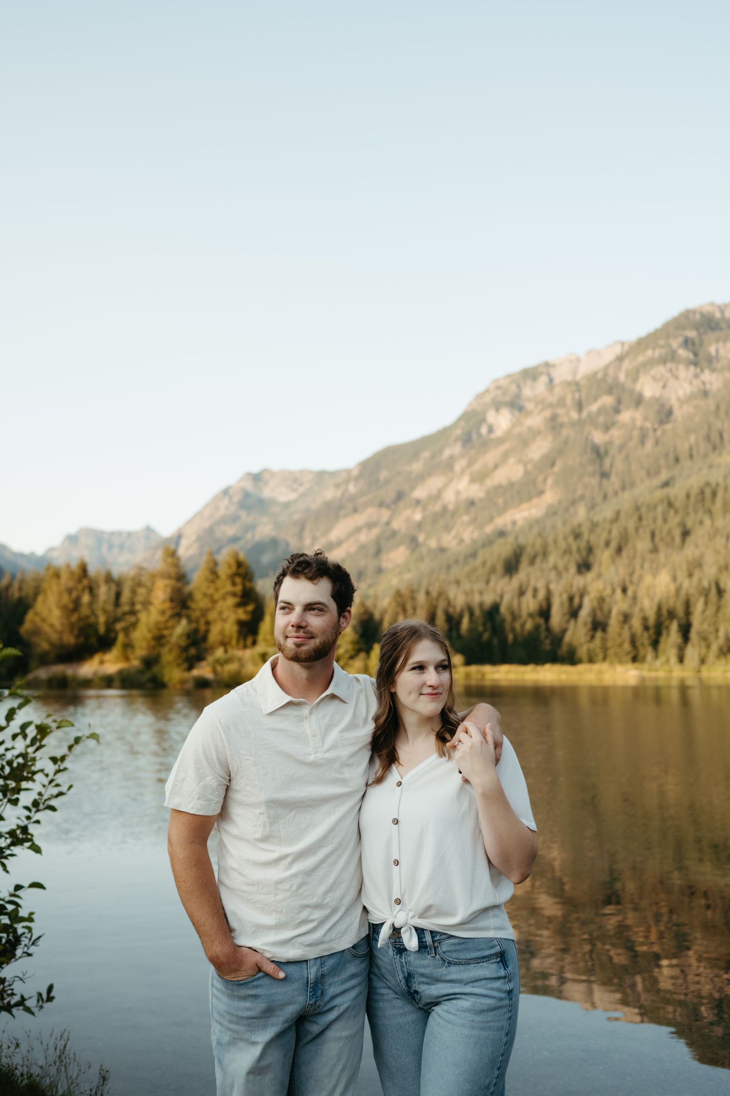 Couple enjoying sunset by mountain lake surrounded by evergreen forest.
