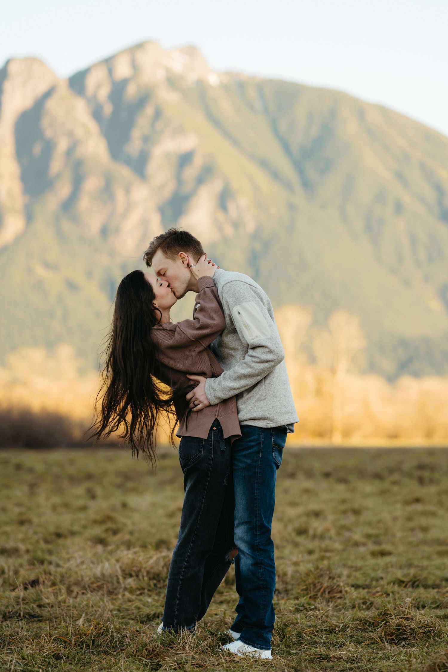 A romantic couple embraces in front of majestic mountain scenery during golden hour.