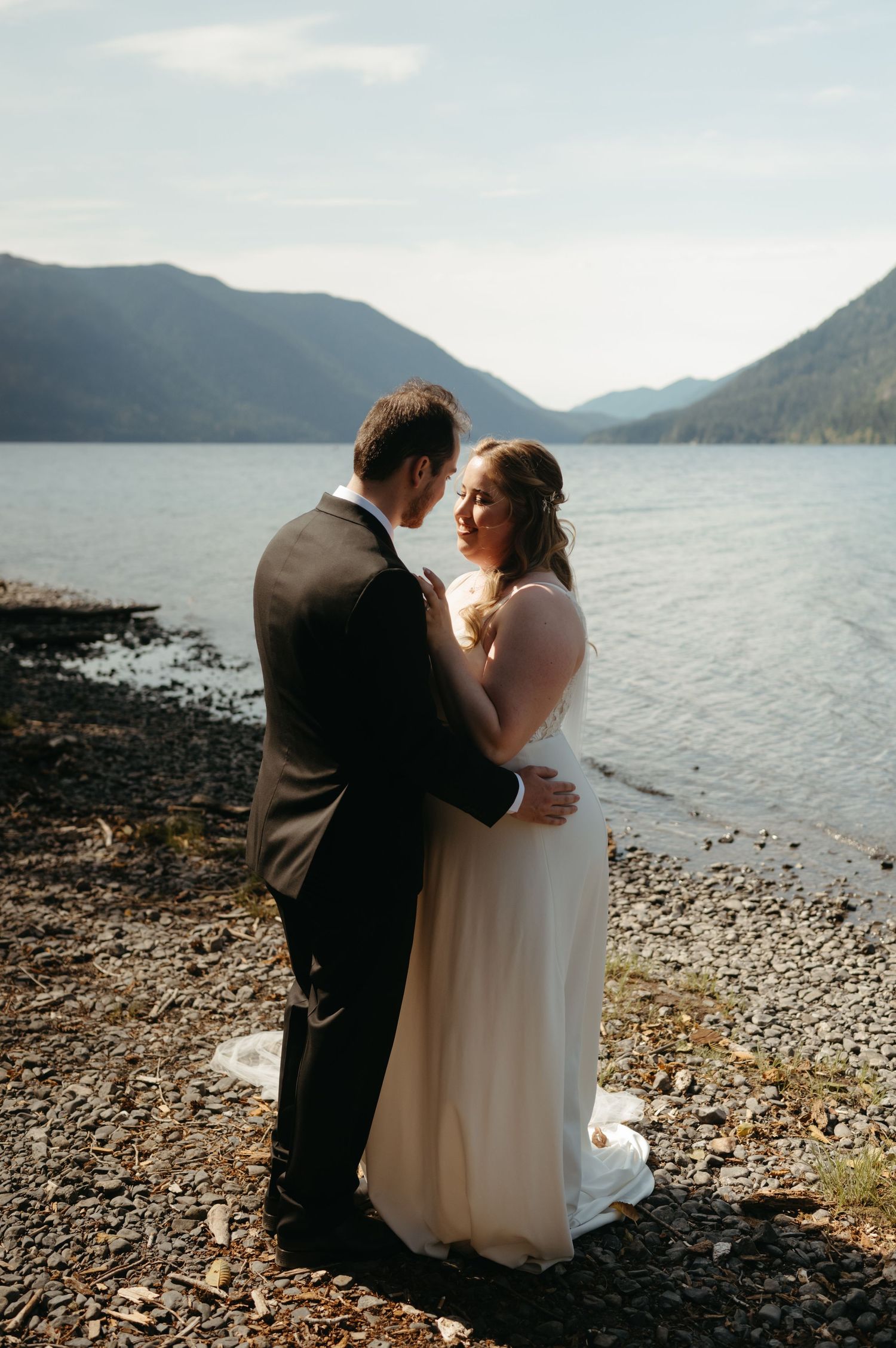 A romantic moment between newlyweds on a lakeside beach with mountain views.