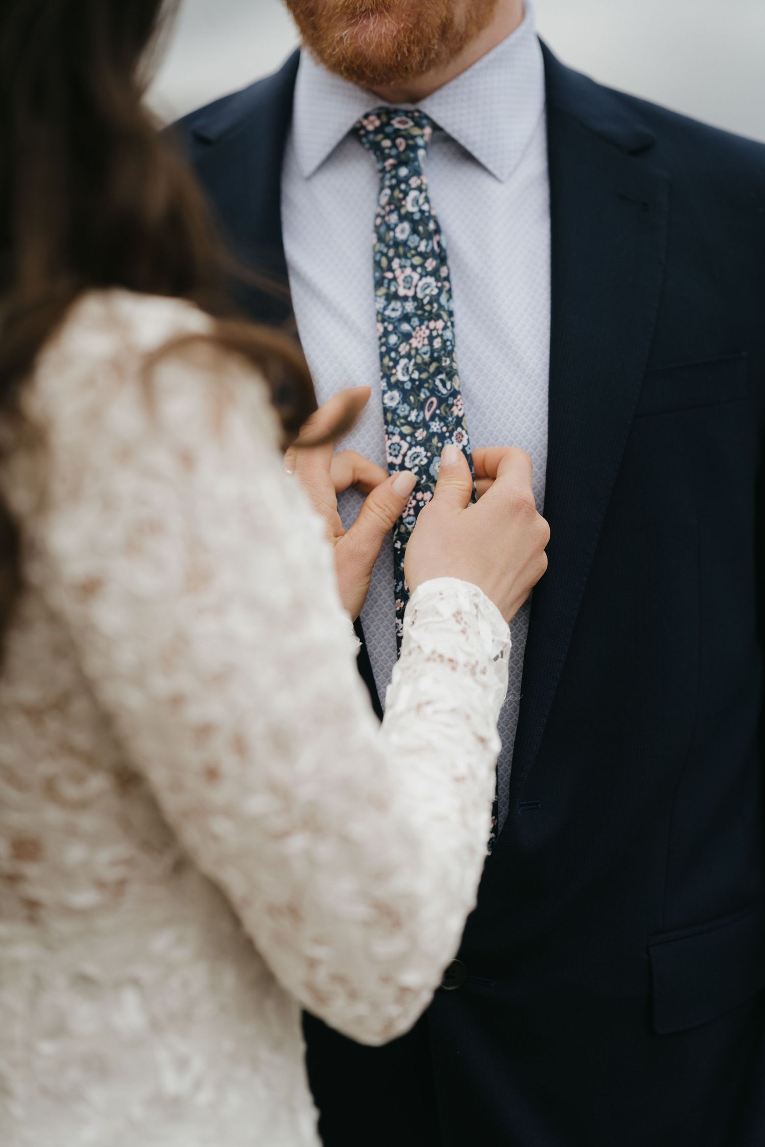 Close-up of hands adjusting a floral tie with lace sleeve detail.