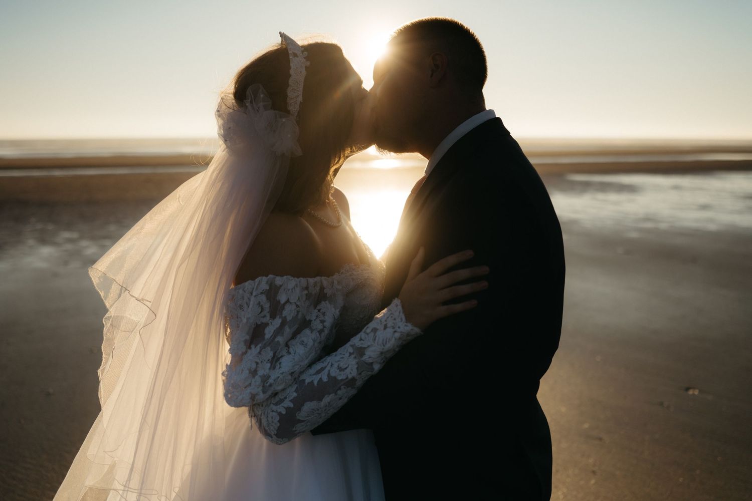 Backlit silhouettes embrace during golden hour on a serene beach.
