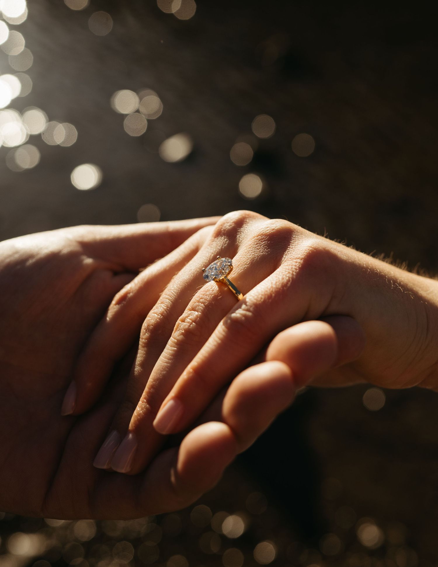 Close up of hands with an engagement ring glinting in bokeh lighting.