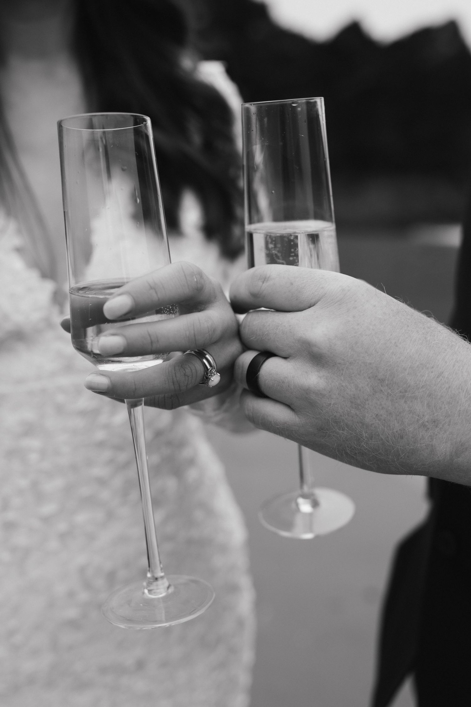 Close-up of champagne glasses clinking in celebration with wedding rings visible.