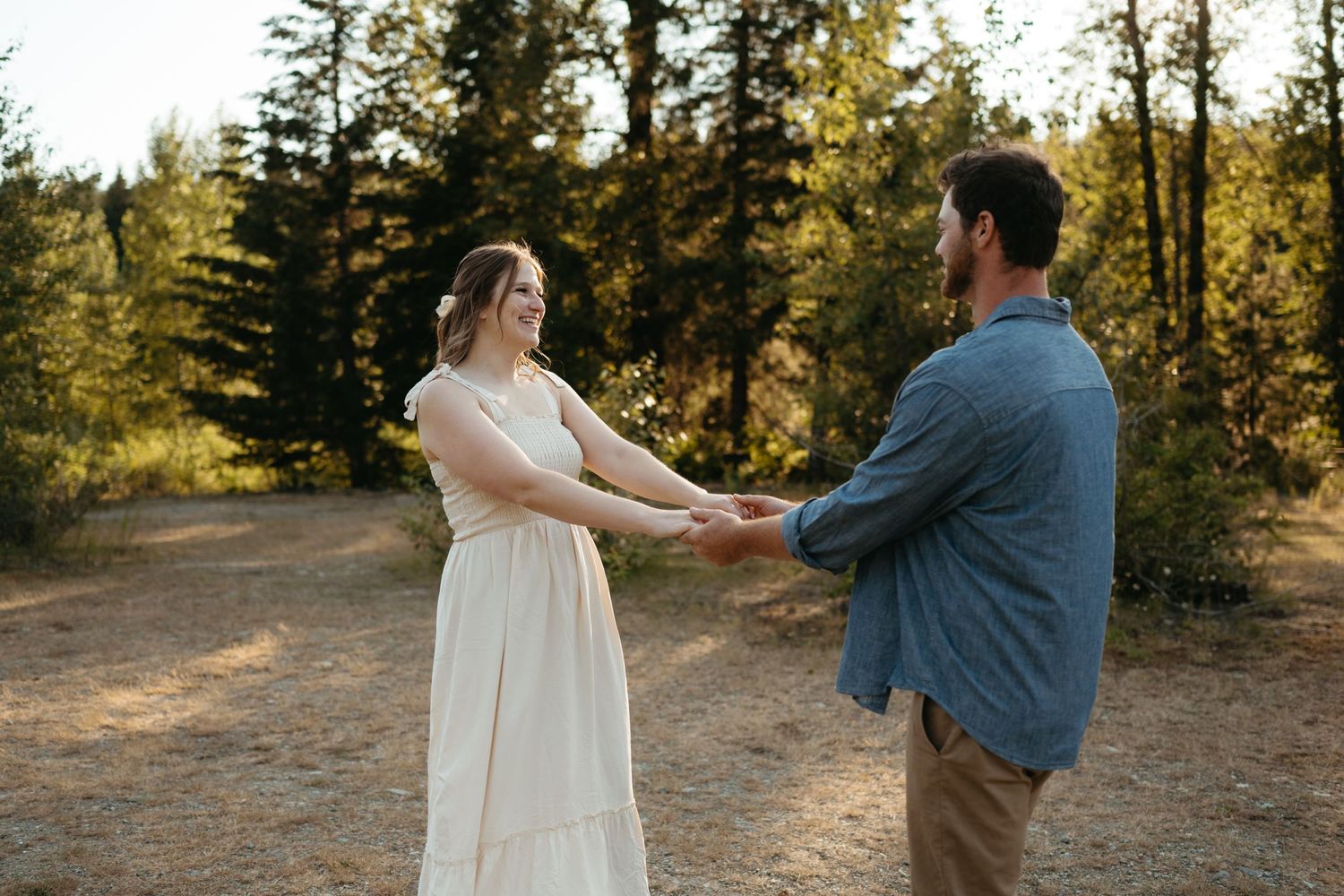Couple holding hands and dancing in a sunlit forest clearing.