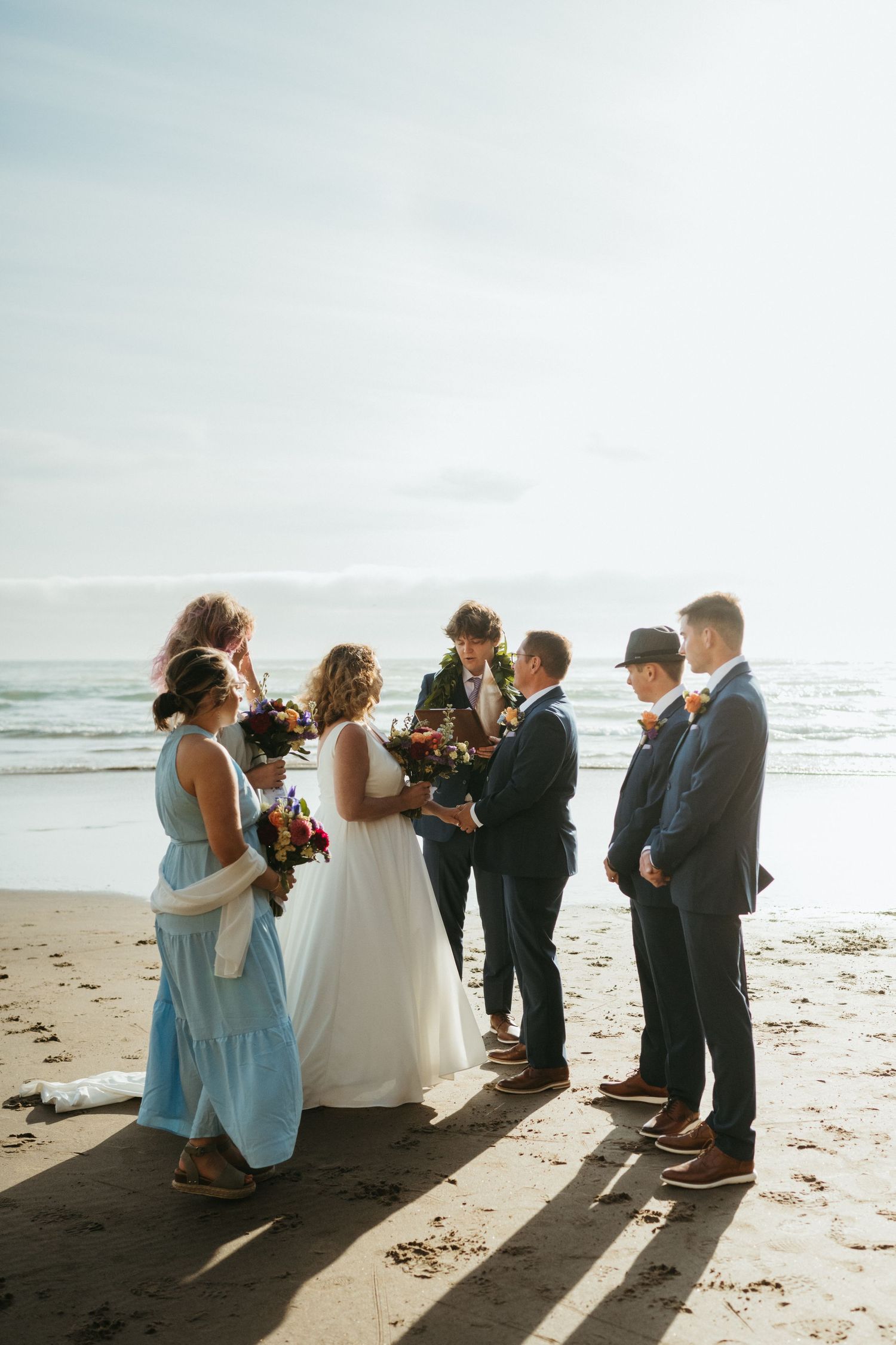 Small wedding group gathered on beach at sunset for intimate ceremony.