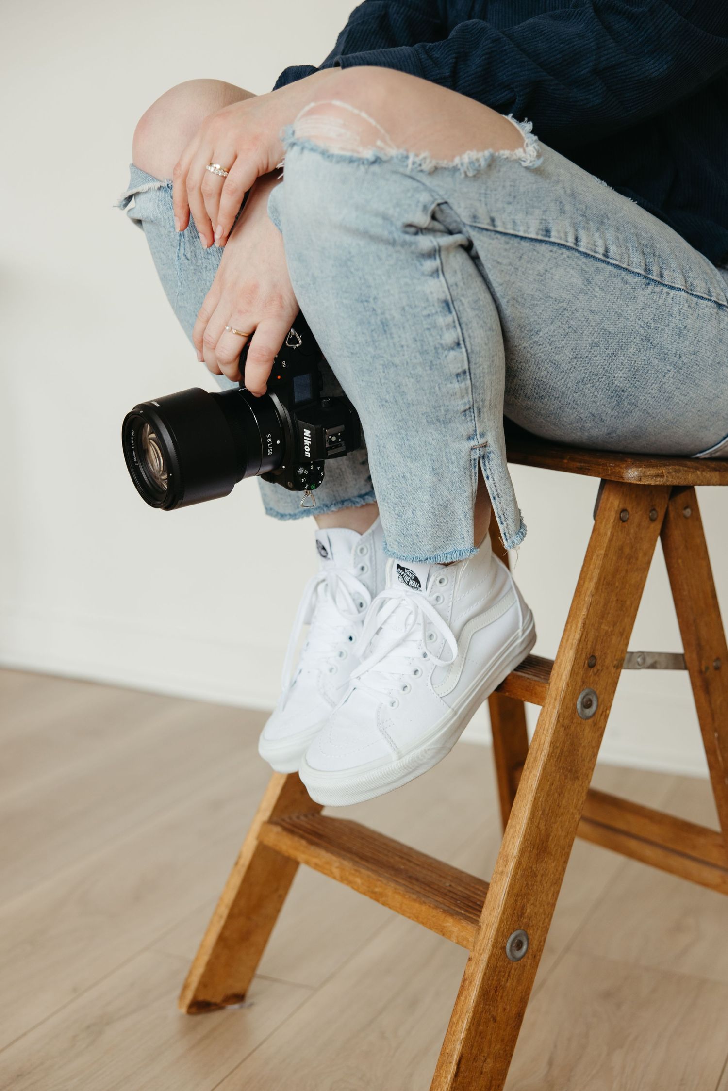Detail shots of white sneakers and ripped jeans on wooden stool with camera.
