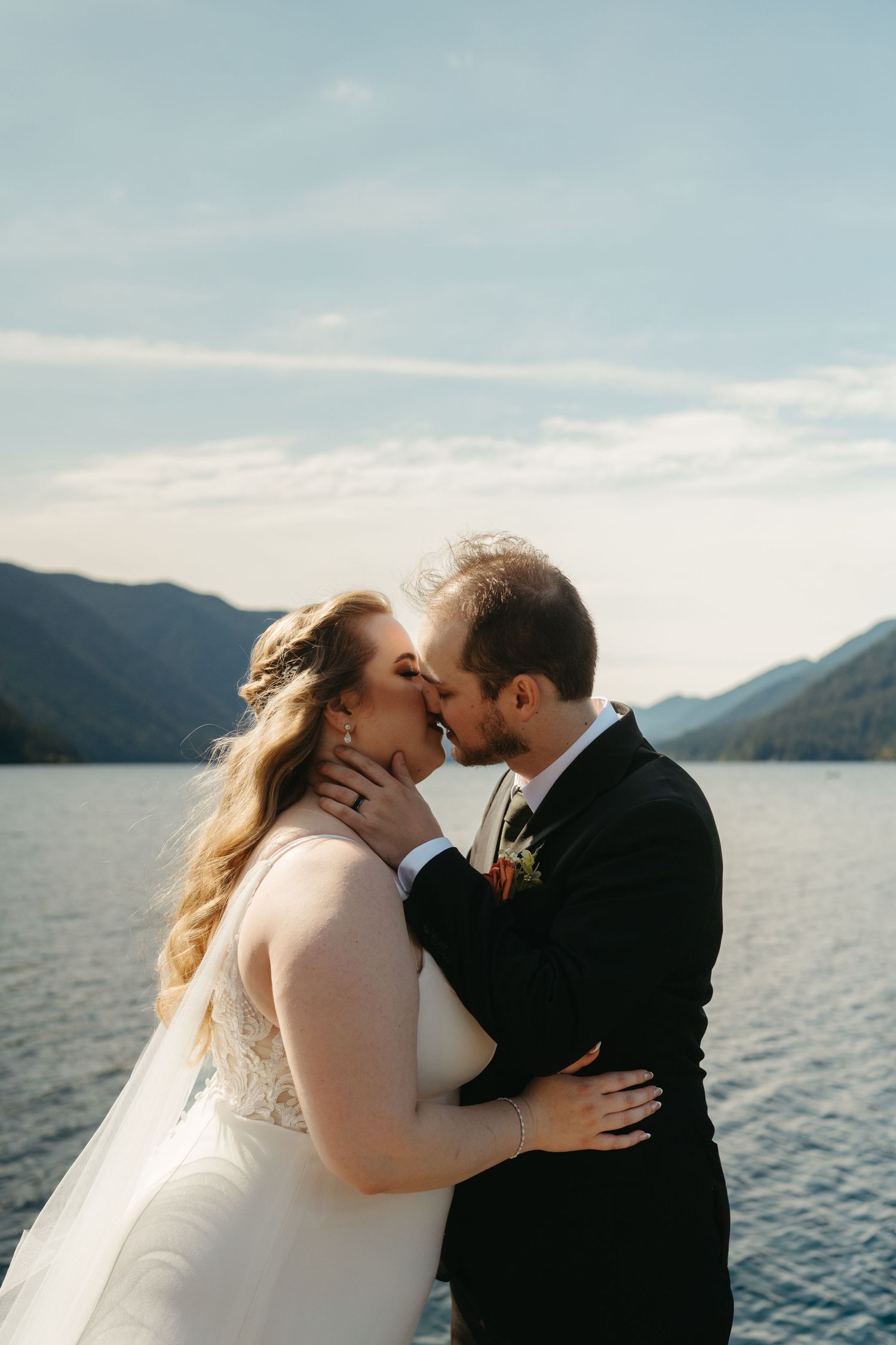 A romantic lakeside wedding moment with mountains visible in the background.