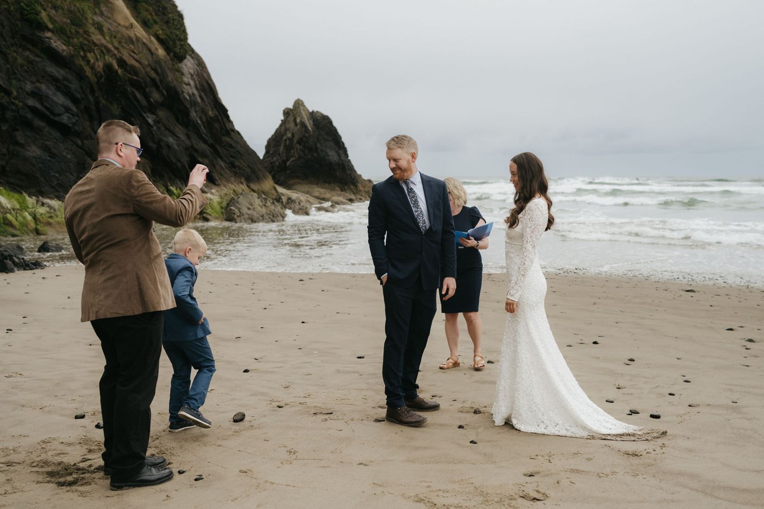 A small group gathers for a beach wedding ceremony with dramatic coastal cliffs behind them.