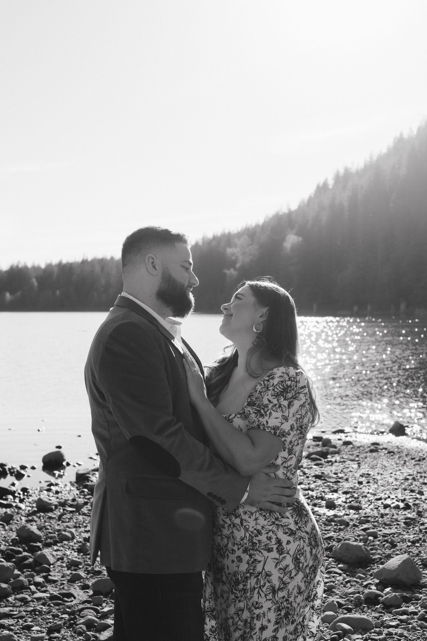 A romantic black and white portrait of a couple embracing on a rocky lakeshore.