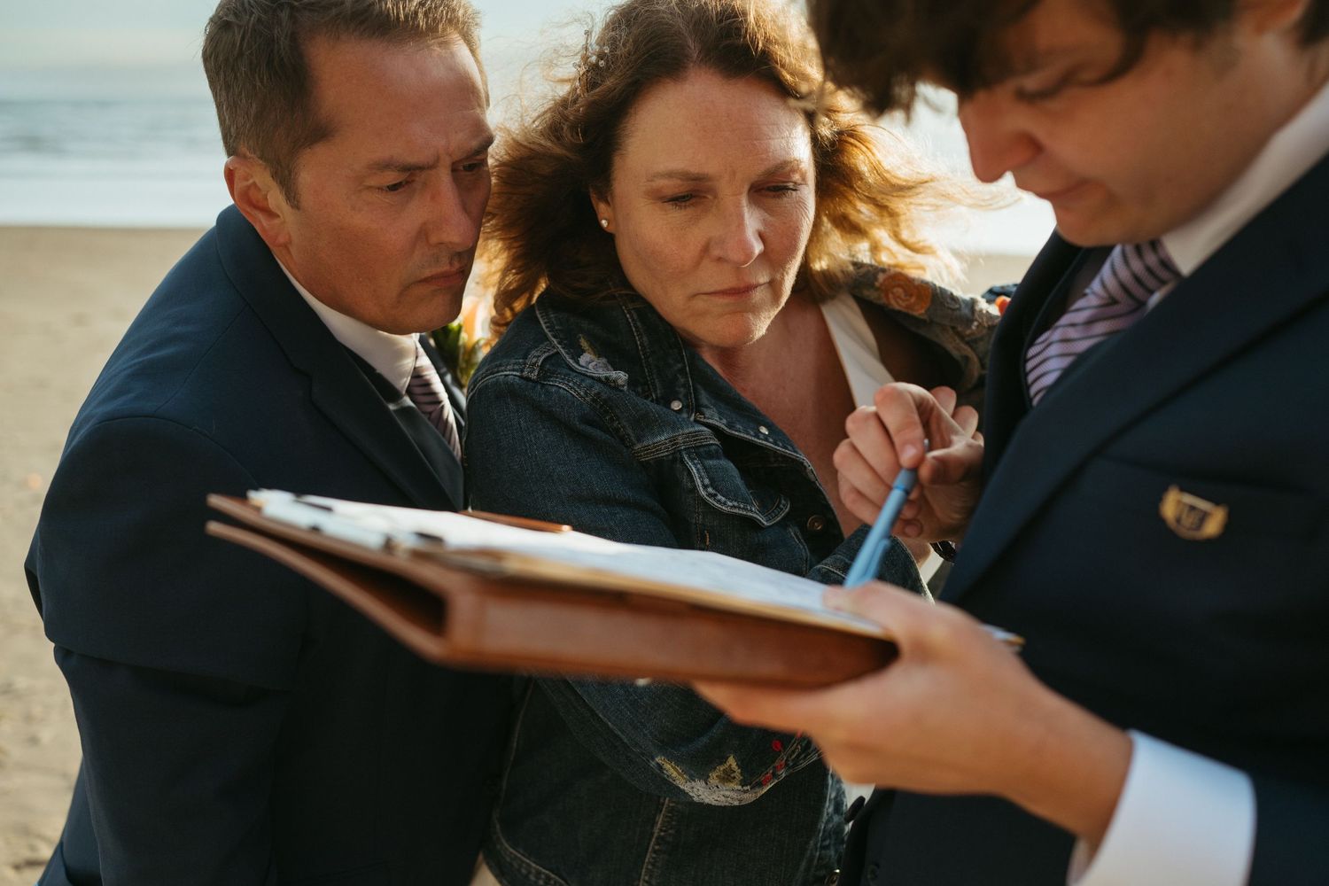 Wedding ceremony documents being signed on a beach with witnesses.