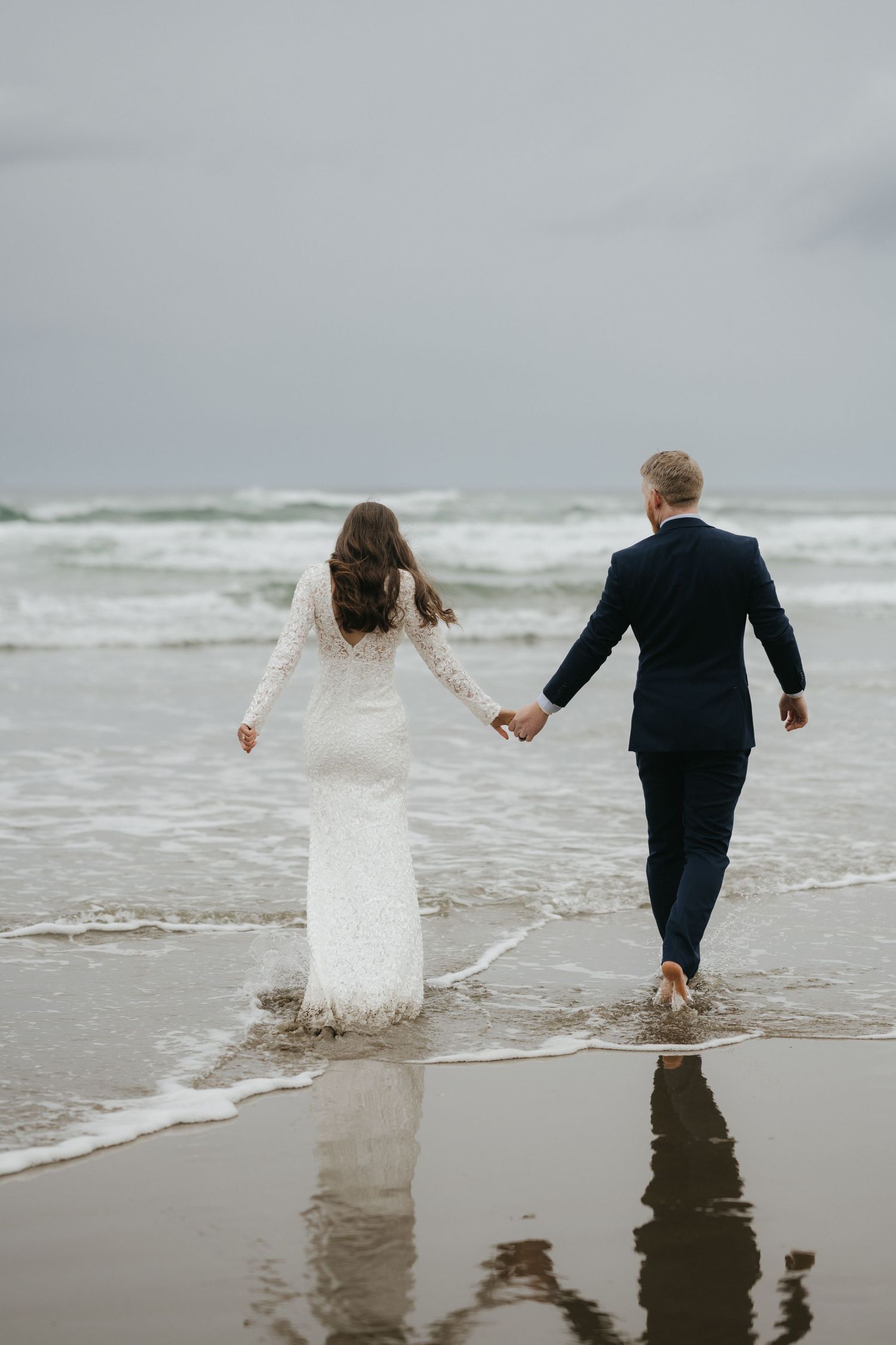 Couple wading in ocean waves during beach wedding photoshoot.