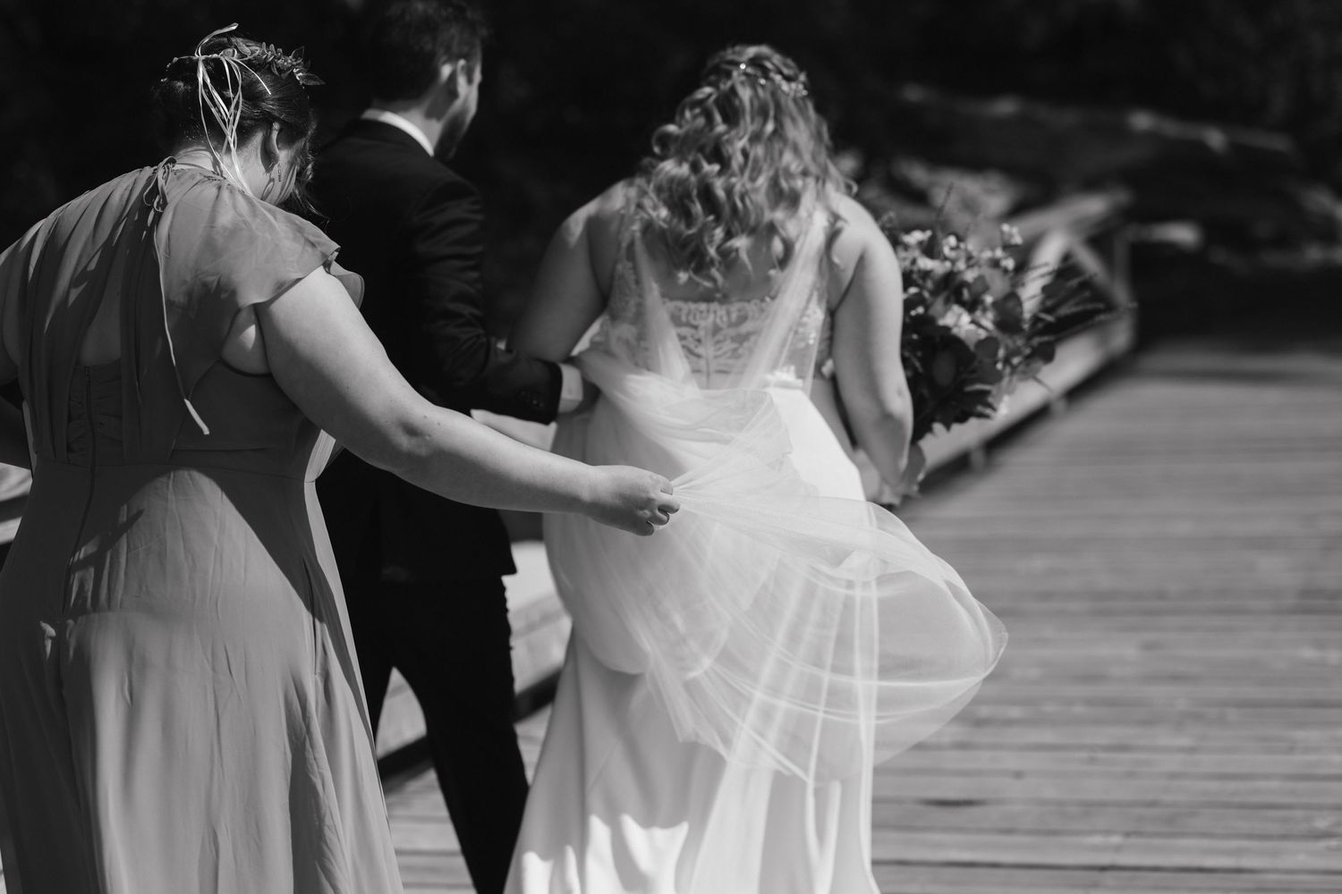 Black and white image of wedding dress details being adjusted on a dock.