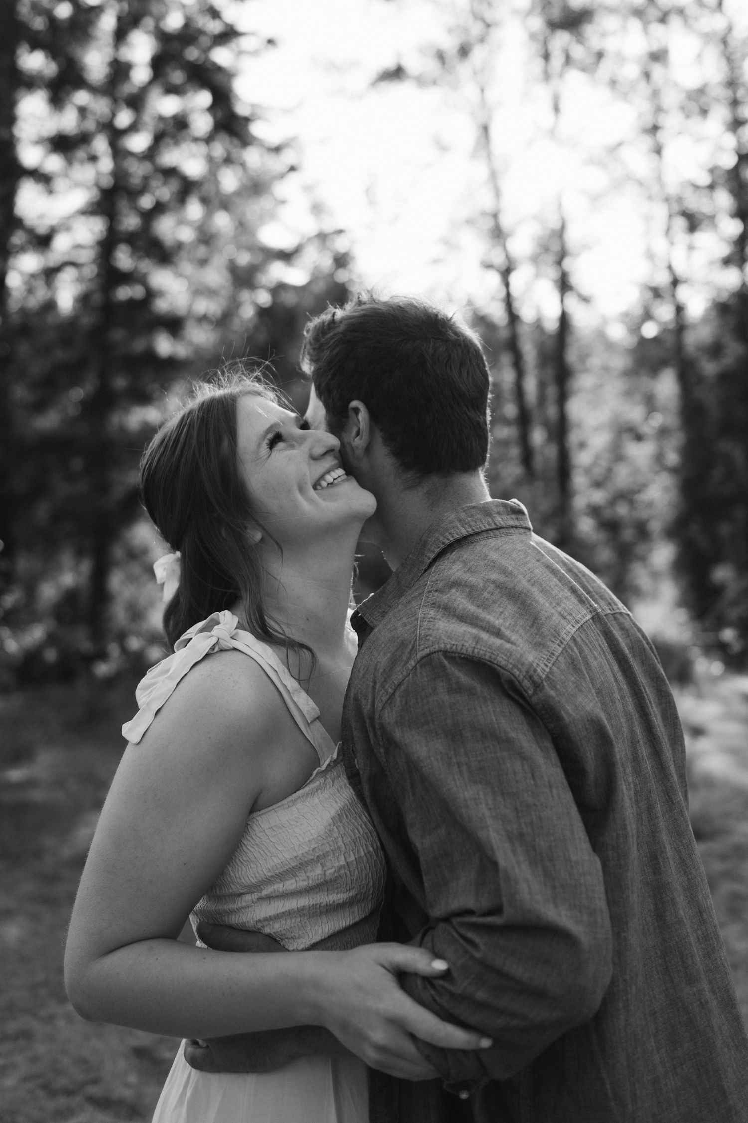 Black and white portrait of a joyful couple embracing outdoors with natural forest backdrop.