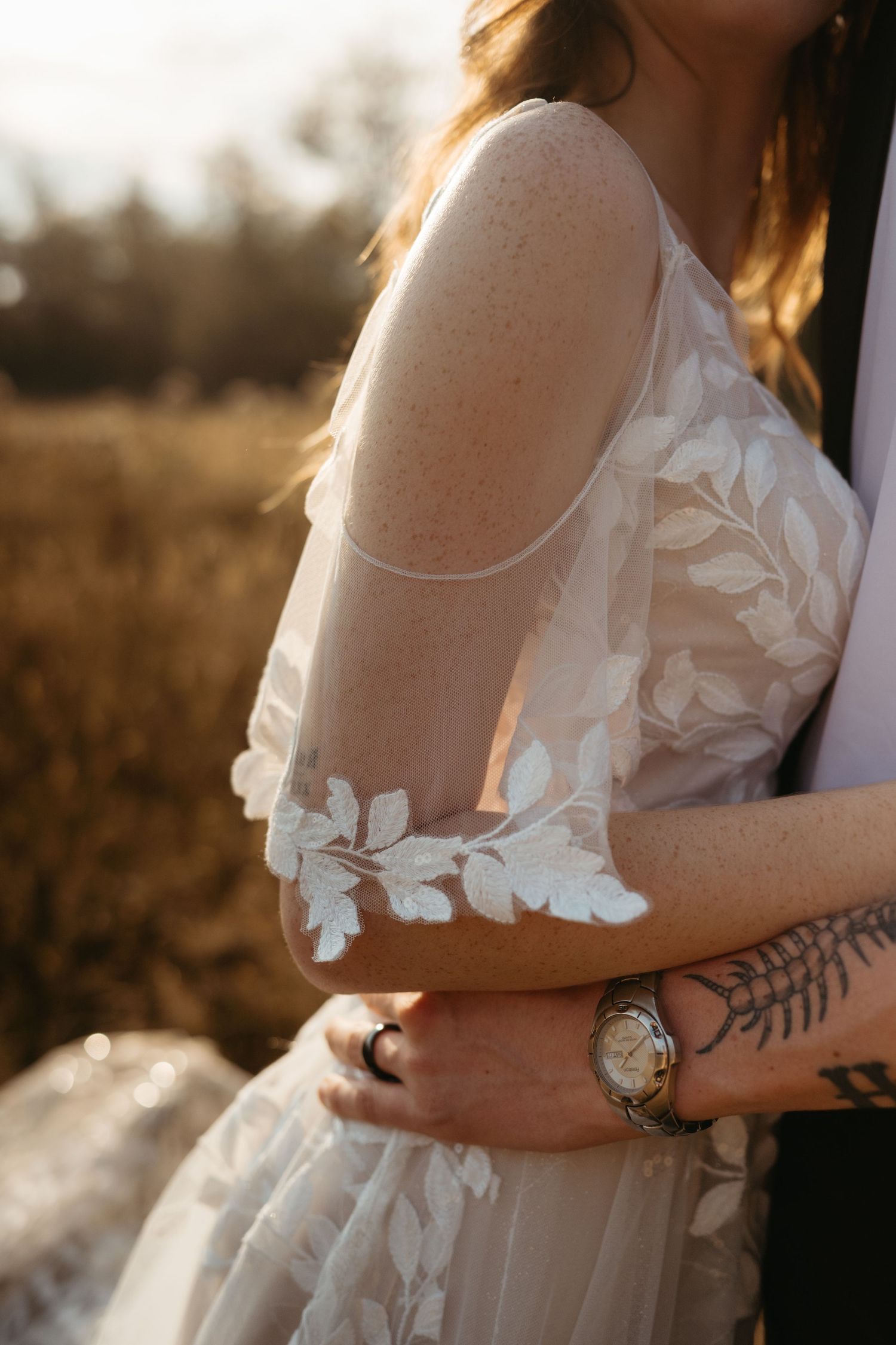 Close-up detail of lace wedding dress with floral pattern in golden sunlight.
