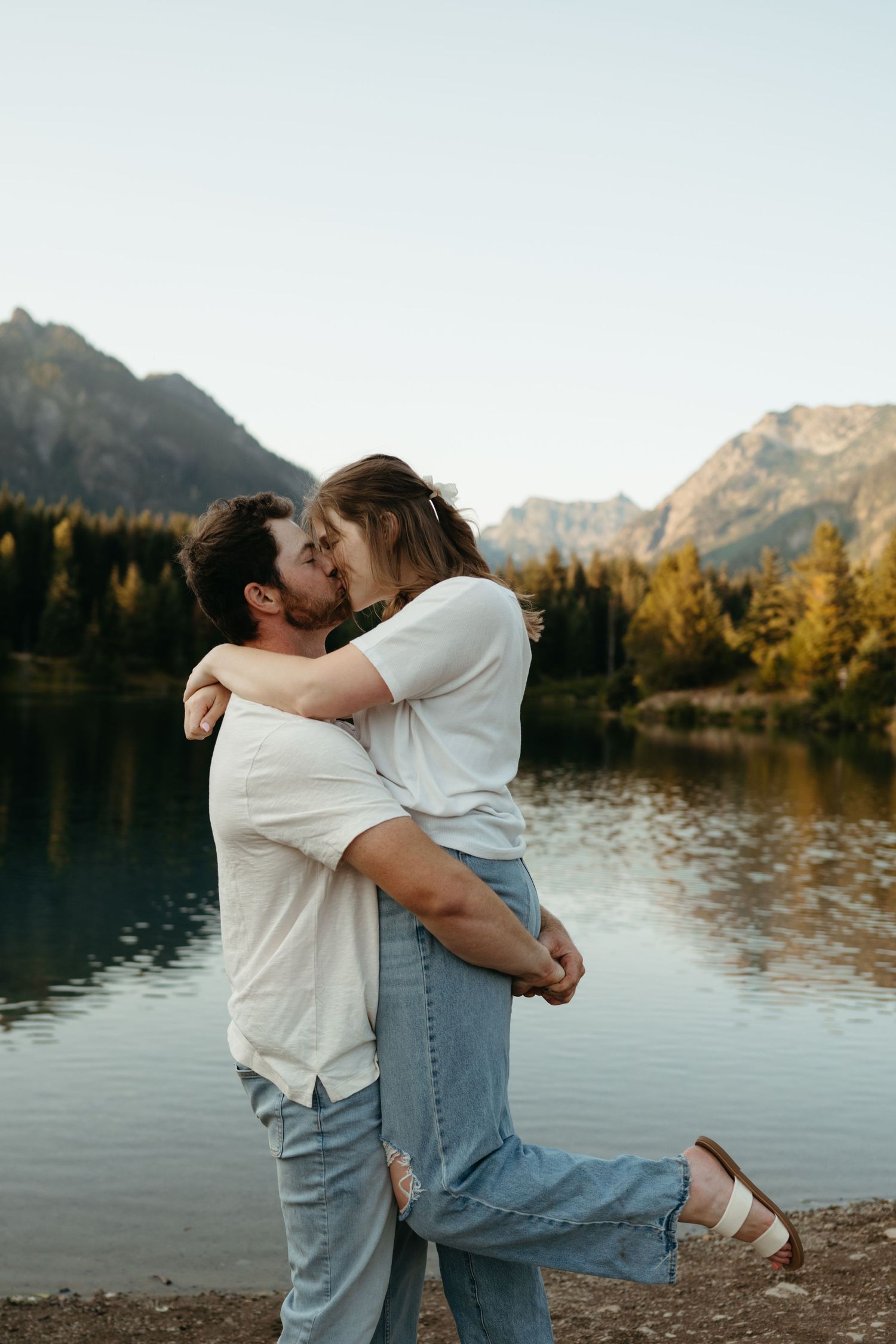 Intimate moment captured at sunset by mountain lake with evergreen trees.