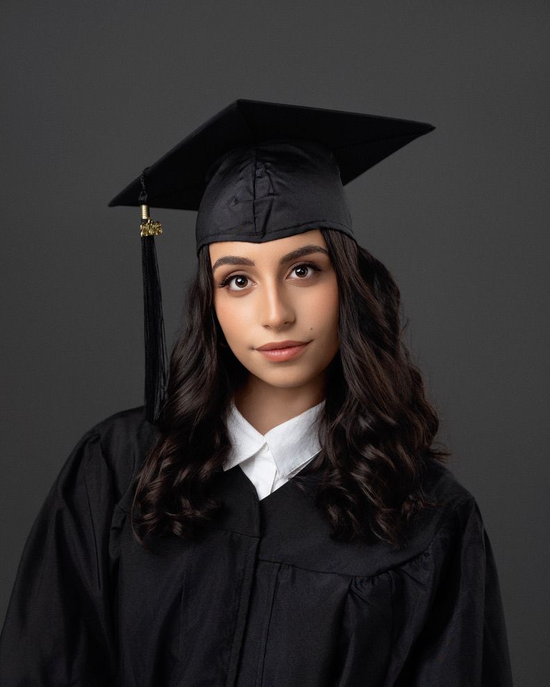 Young woman in black graduation cap and gown posing for a professional portrait against a gray background.