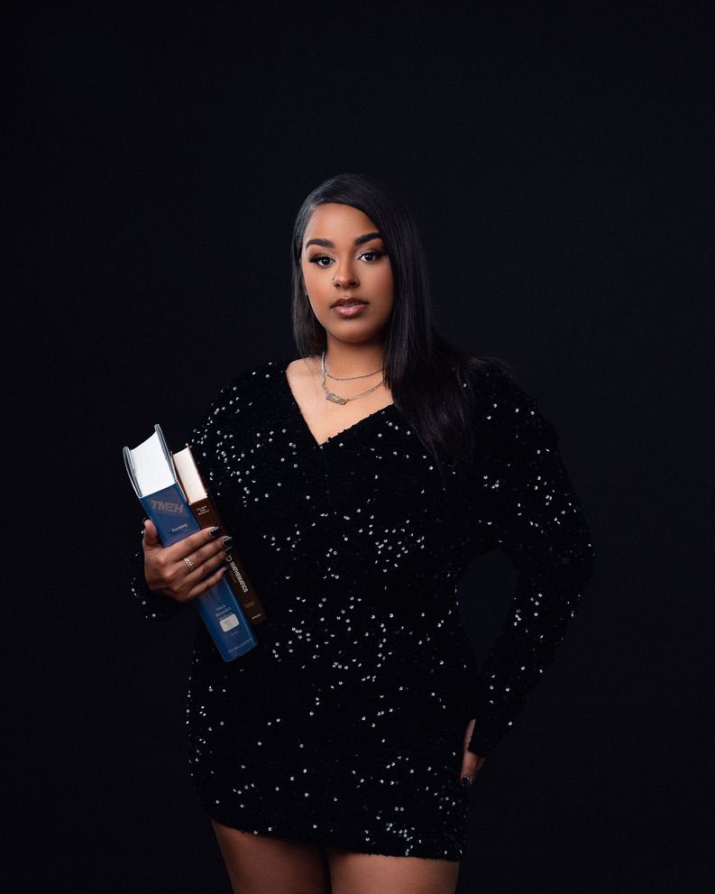 Woman in black sequin mini dress holding an award trophy, posing against dark background.