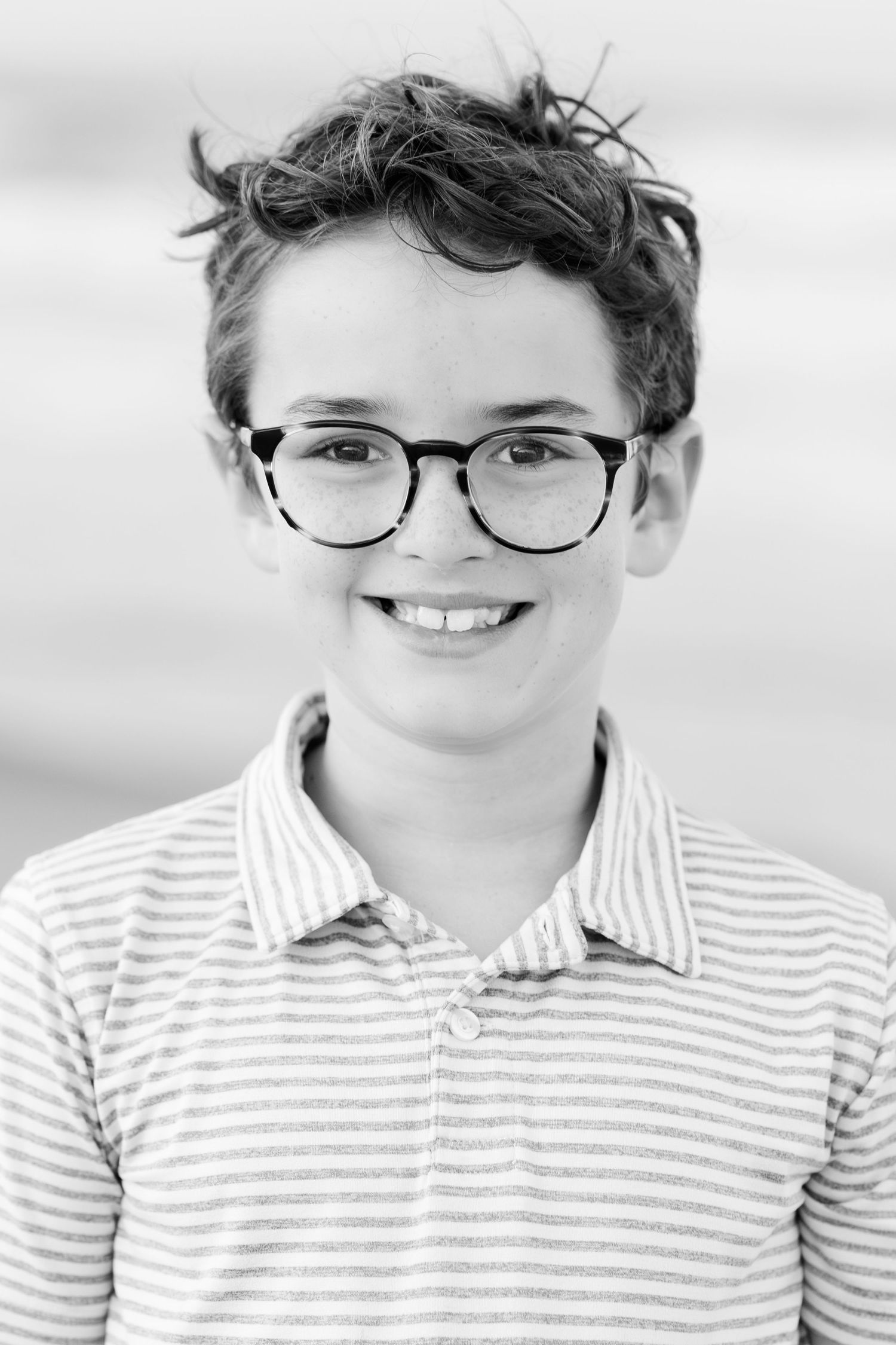Black and white headshot of a youth wearing glasses and a striped polo shirt.