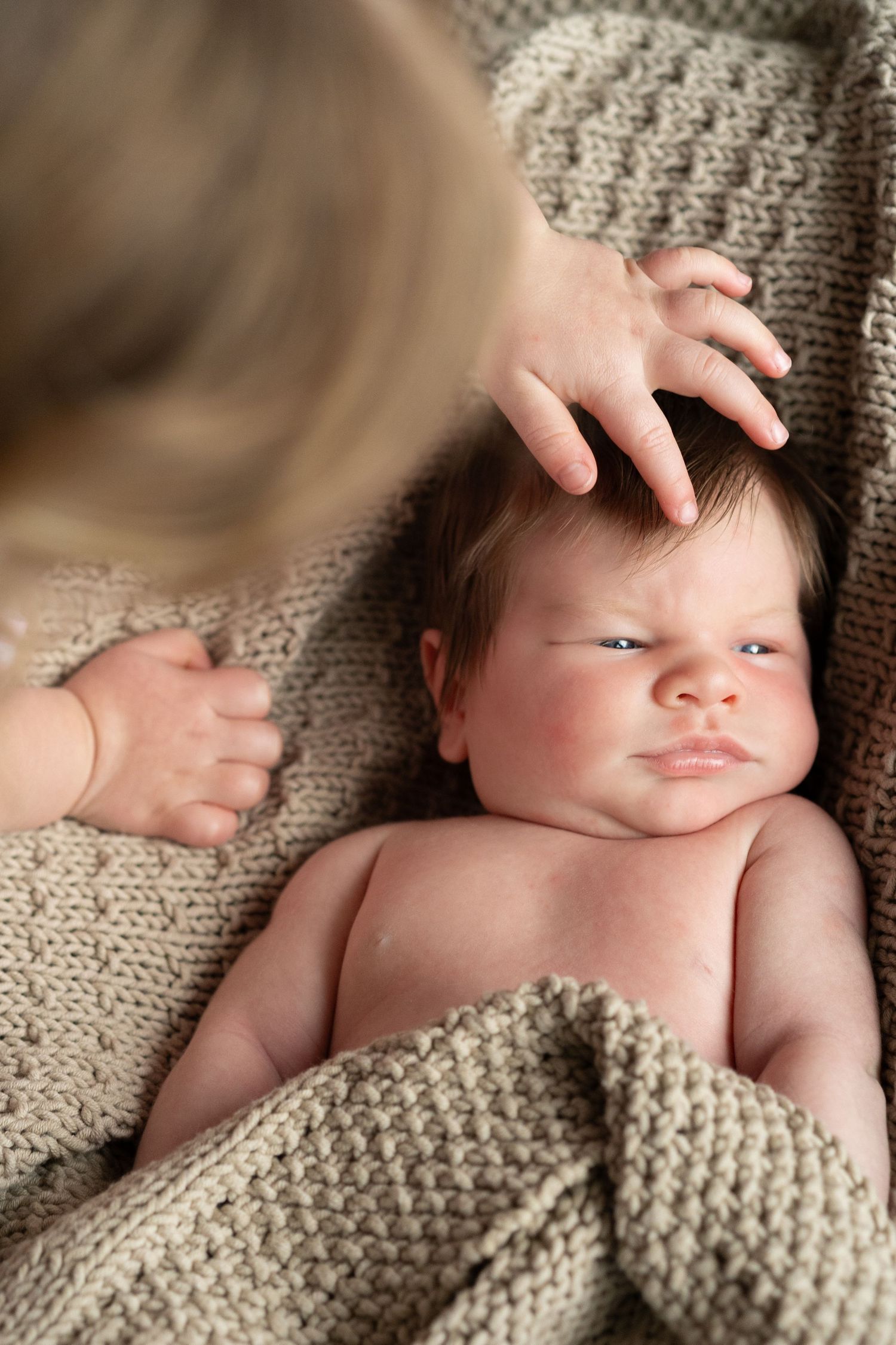 Infant portrait with gentle hand touch against textured knit background.