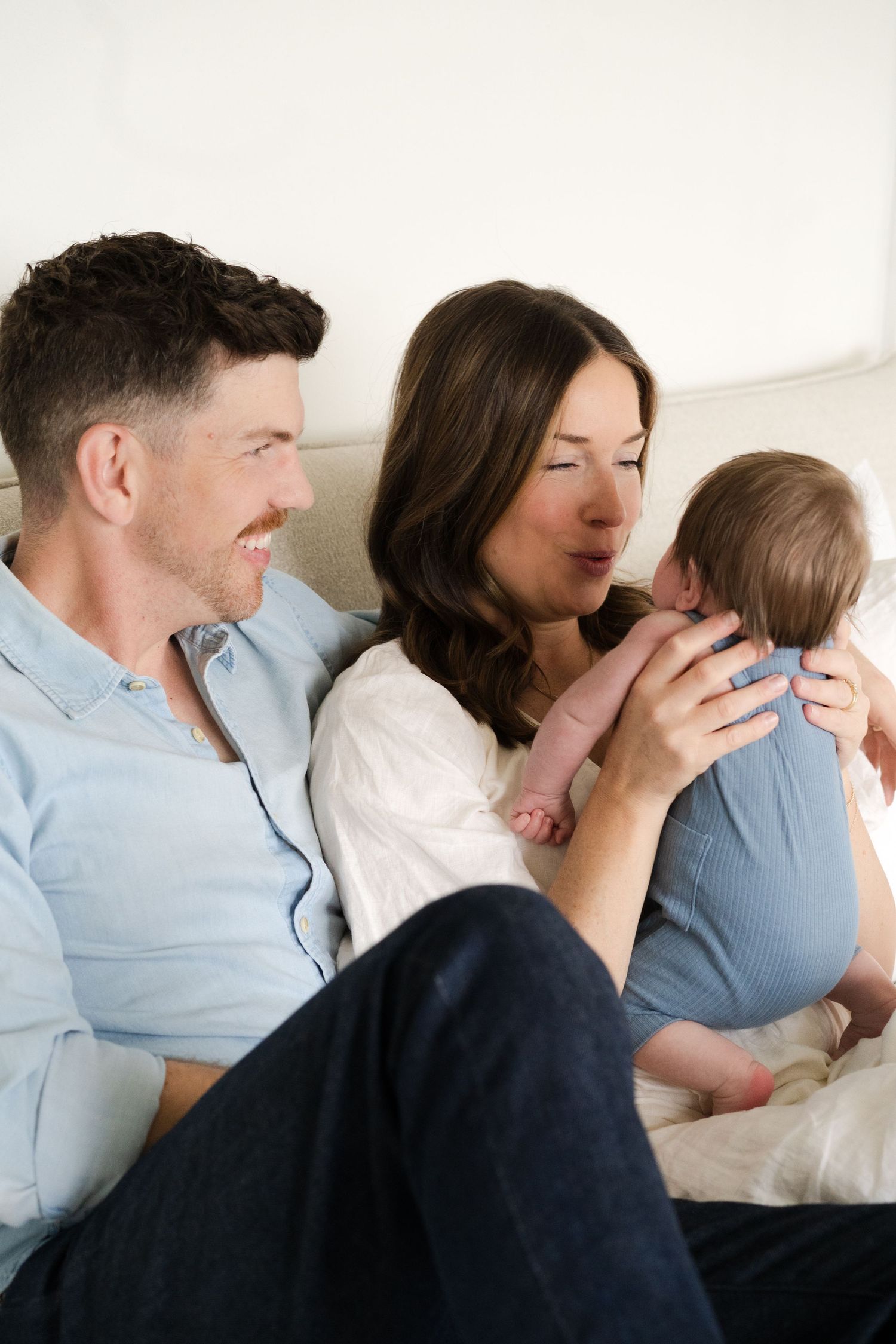 Family portrait series showing candid moments of parents and child interacting on a white couch.