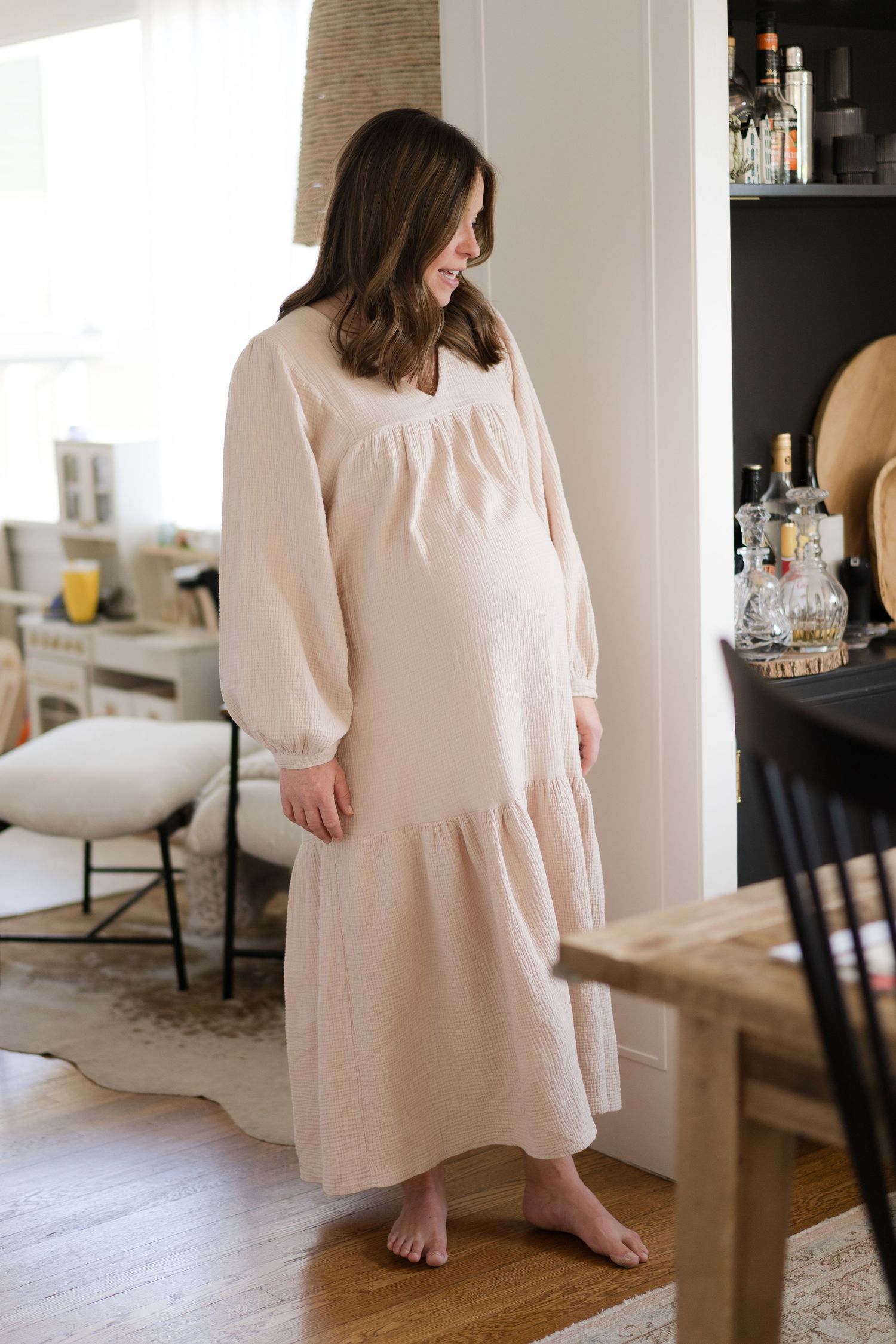 Woman in flowing cream dress twirls in bright modern living room with hardwood floors.