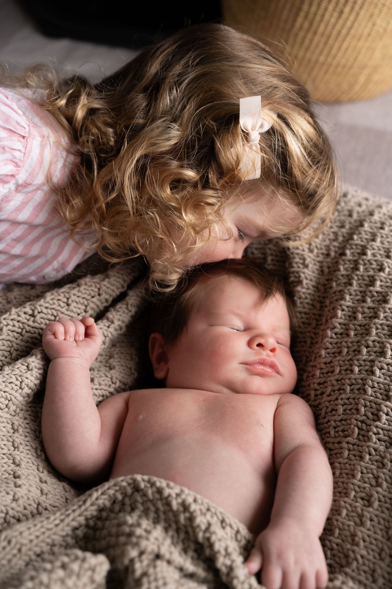 Child resting peacefully on textured beige blanket with natural lighting.
