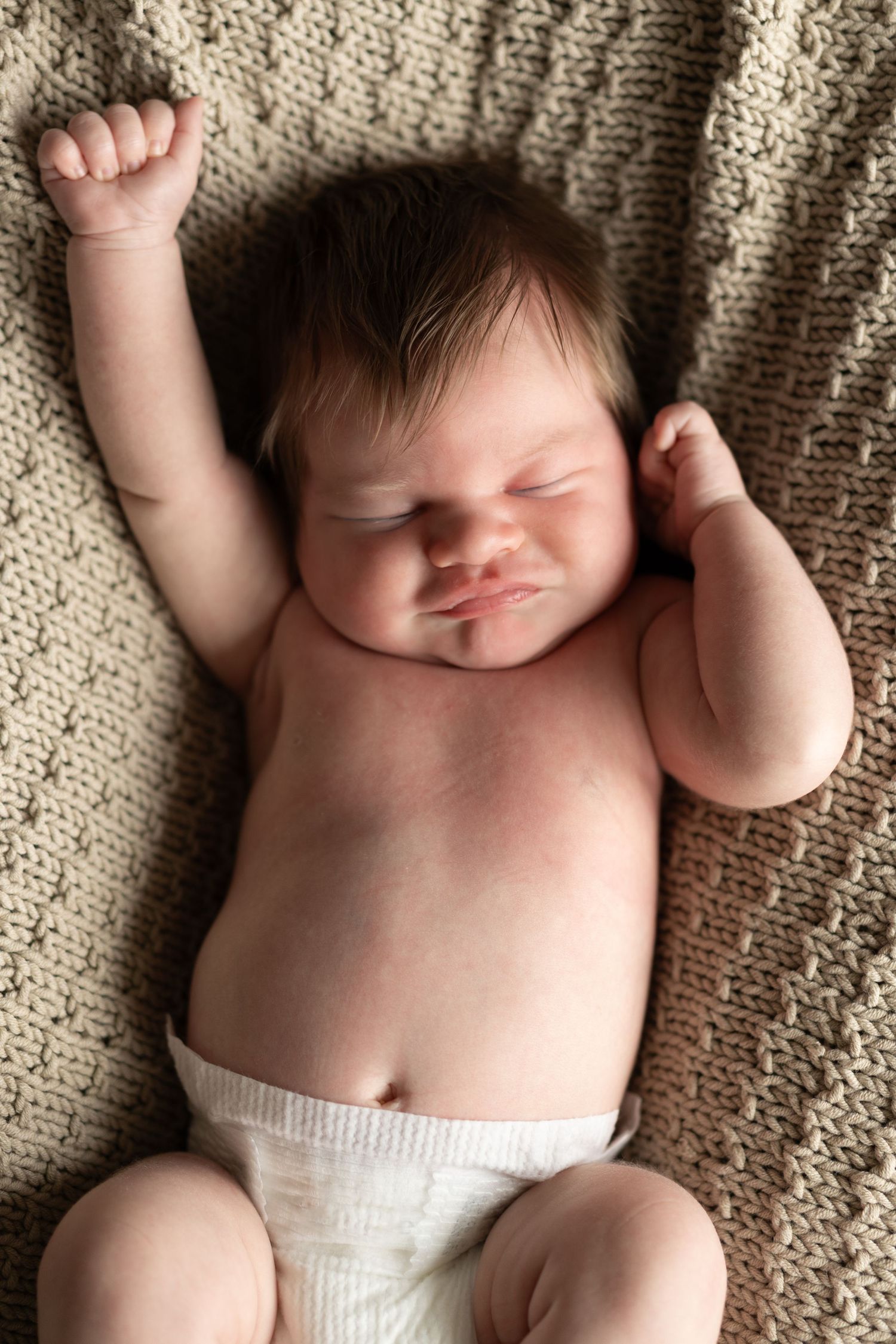 Newborn baby sleeping peacefully on a knitted beige blanket.