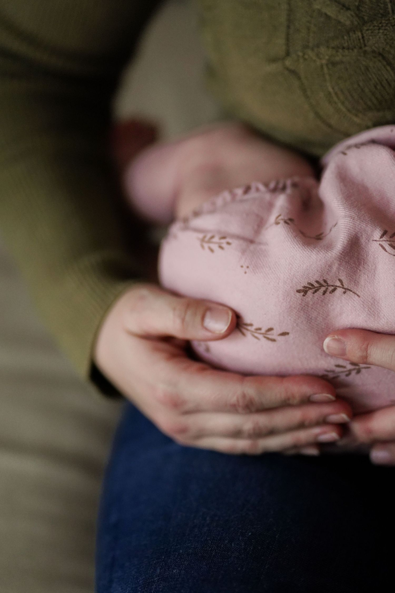 Close-up of tiny baby hands grasping a soft pink fabric with delicate embroidery details.
