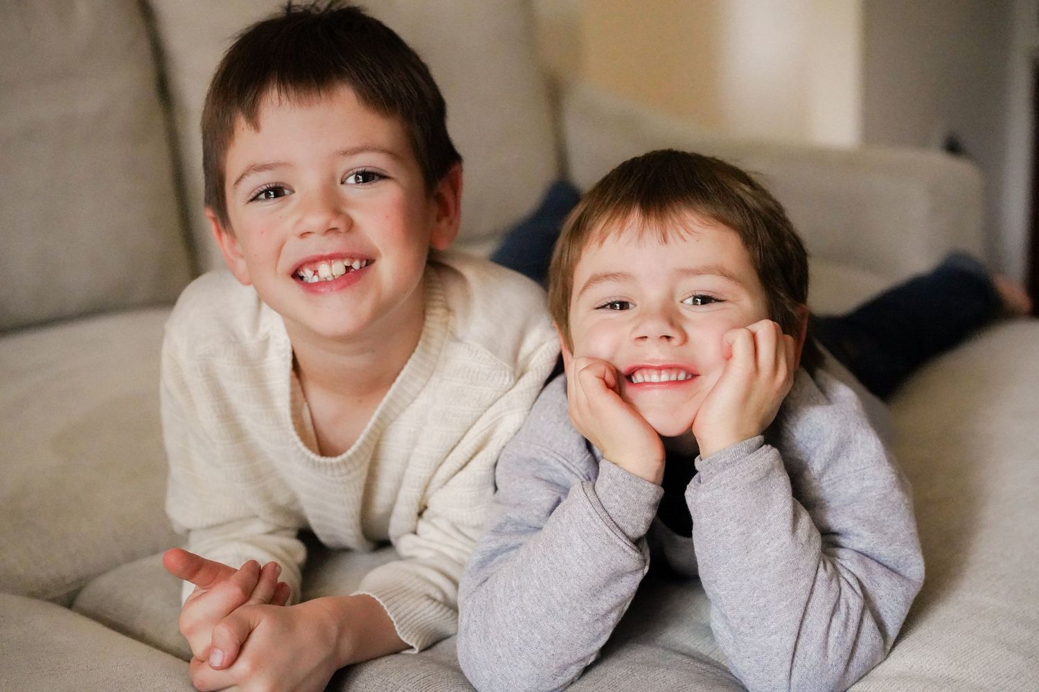 Two children lying on a couch smiling brightly at the camera.